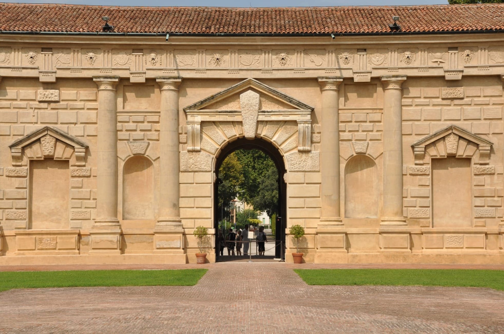 Symmetrical view of an arched portal in the courtyard, where a massive keystone breaks through the triangular pediment.