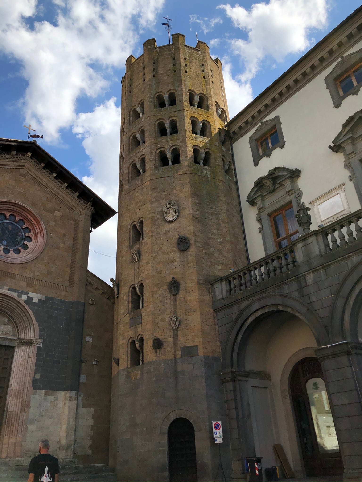 Low-angle shot of the multi-sided stone bell tower of Sant'Andrea with tiers of arched windows, next to a historic palace with an arched loggia.