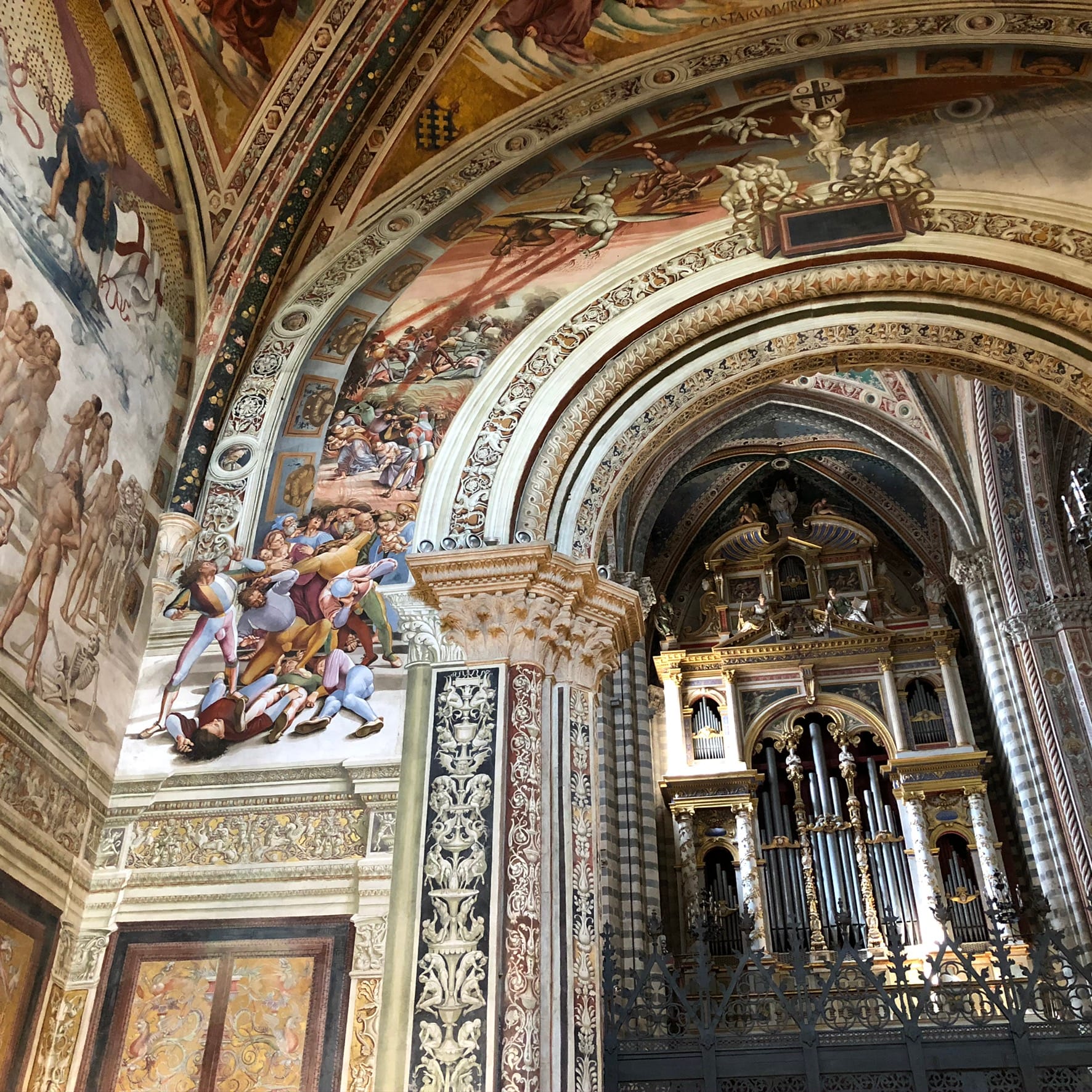 Interior shot looking past a frescoed archway toward a massive, ornate golden pipe organ in the transept, separated by a dark decorative metal gate.