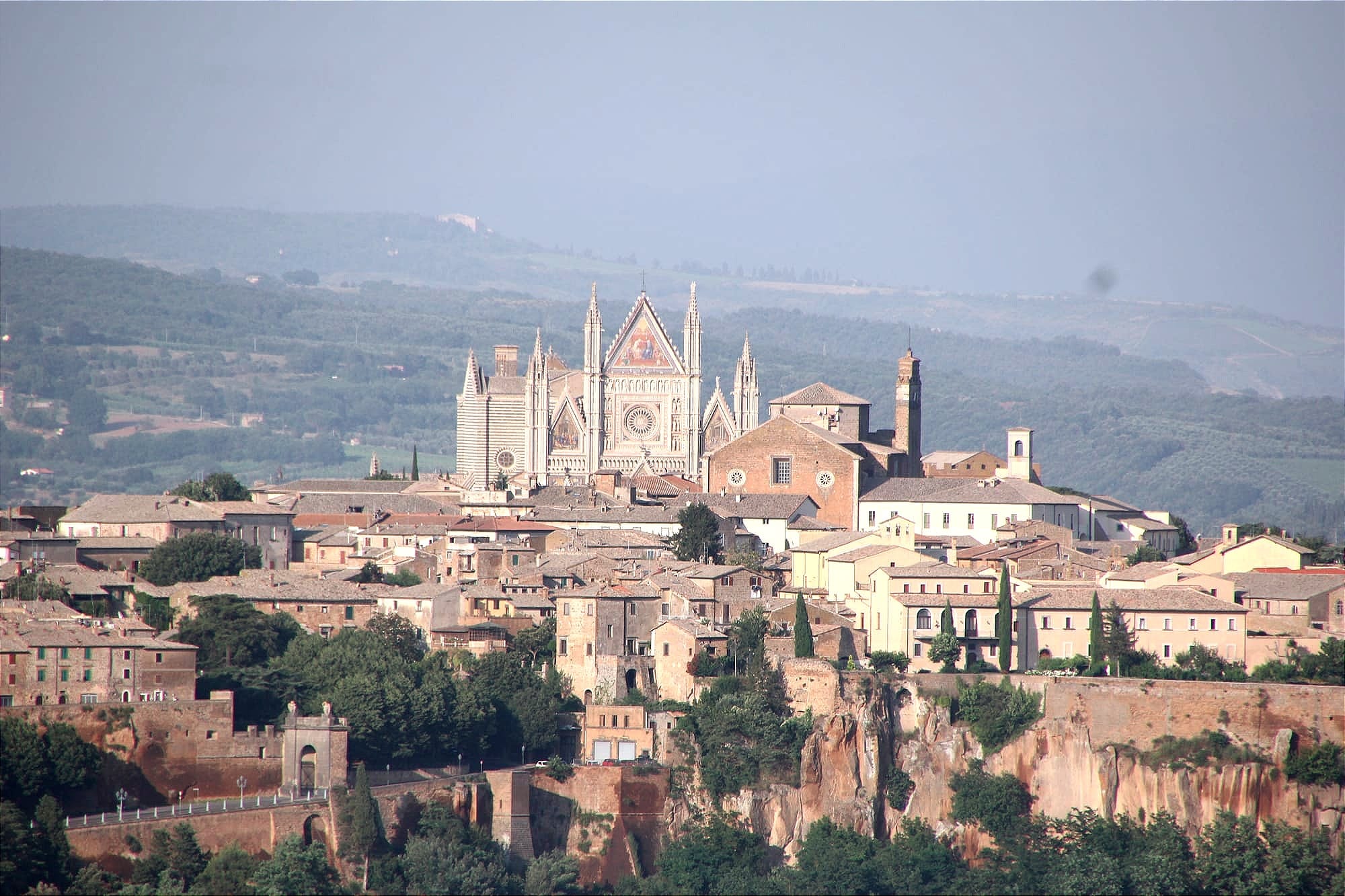 Telephoto view of terracotta roofs in Orvieto's historic center, dominated by the massive plane of the Duomo's screen facade rising high above the town.