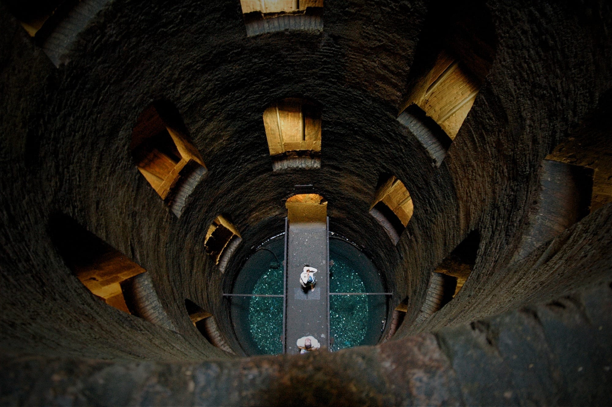 Looking down the circular shaft of St. Patrick's Well. Rows of arched windows illuminate the double-helix stairs leading to a small bridge at the bottom.