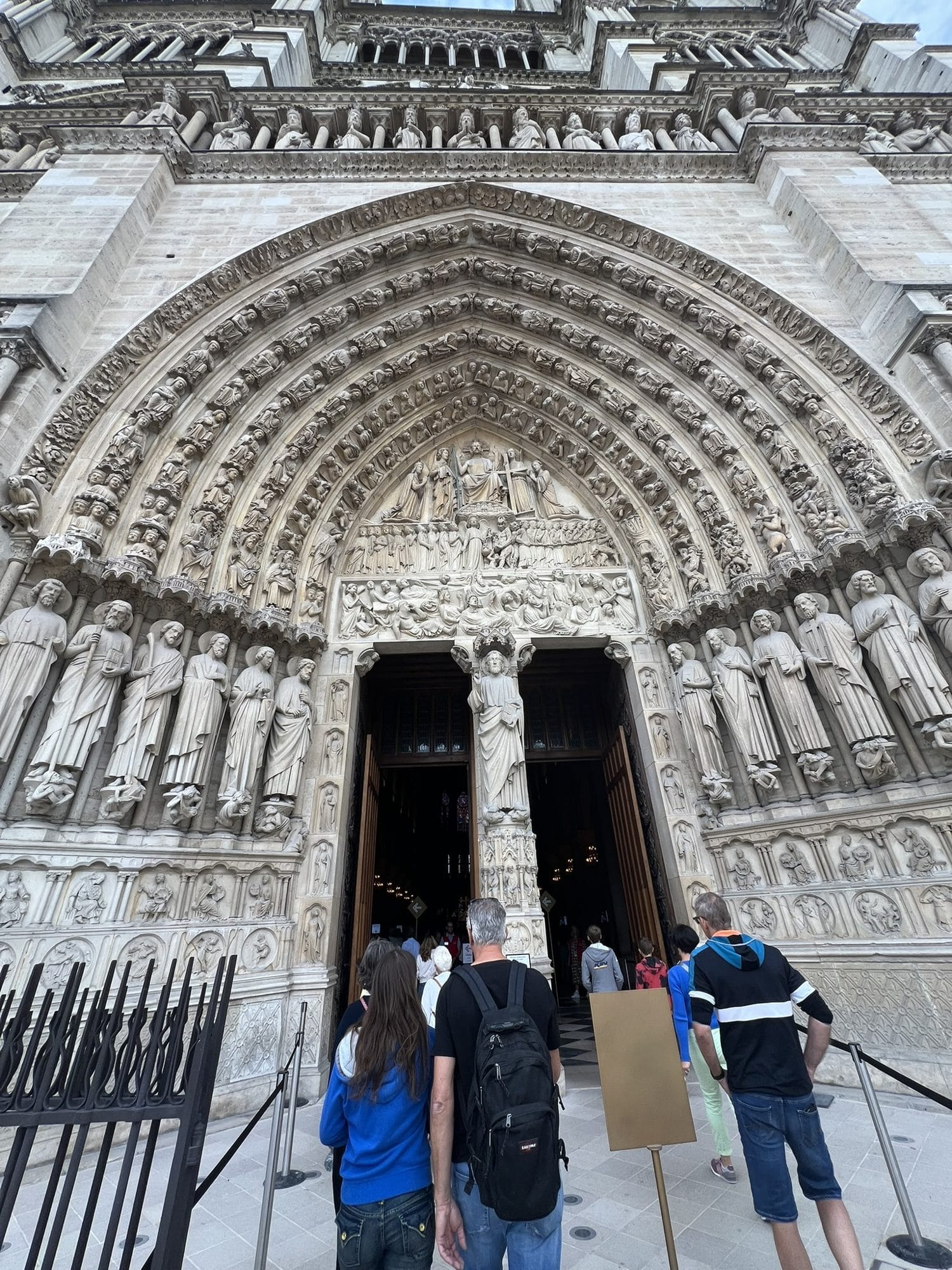 Visitors seen from behind queuing at the carved central portal of Notre-Dame de Paris