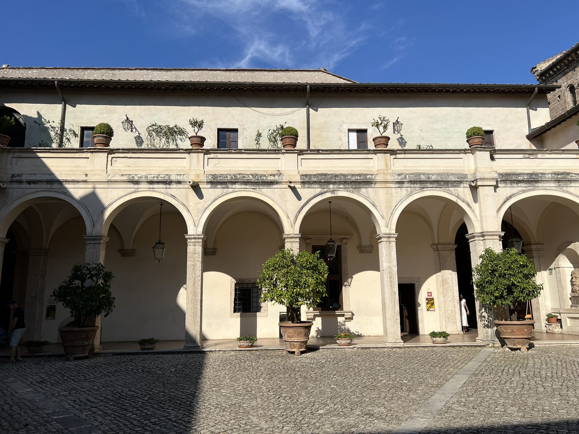 Courtyard with an arcaded portico, potted citrus trees and an upper loggia under a blue sky