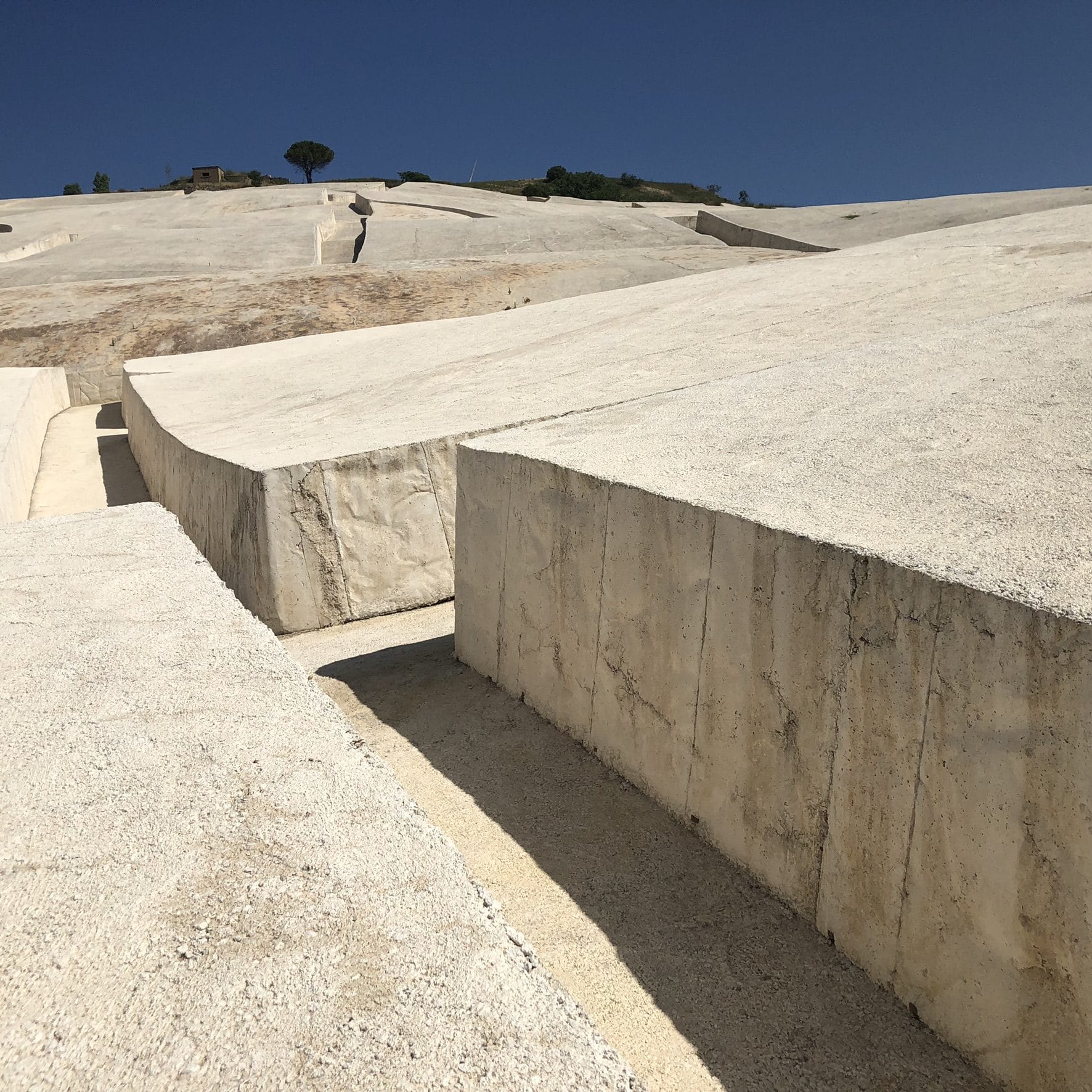Massive white concrete blocks of the Cretto separated by narrow walkways, with sharp shadows on one side