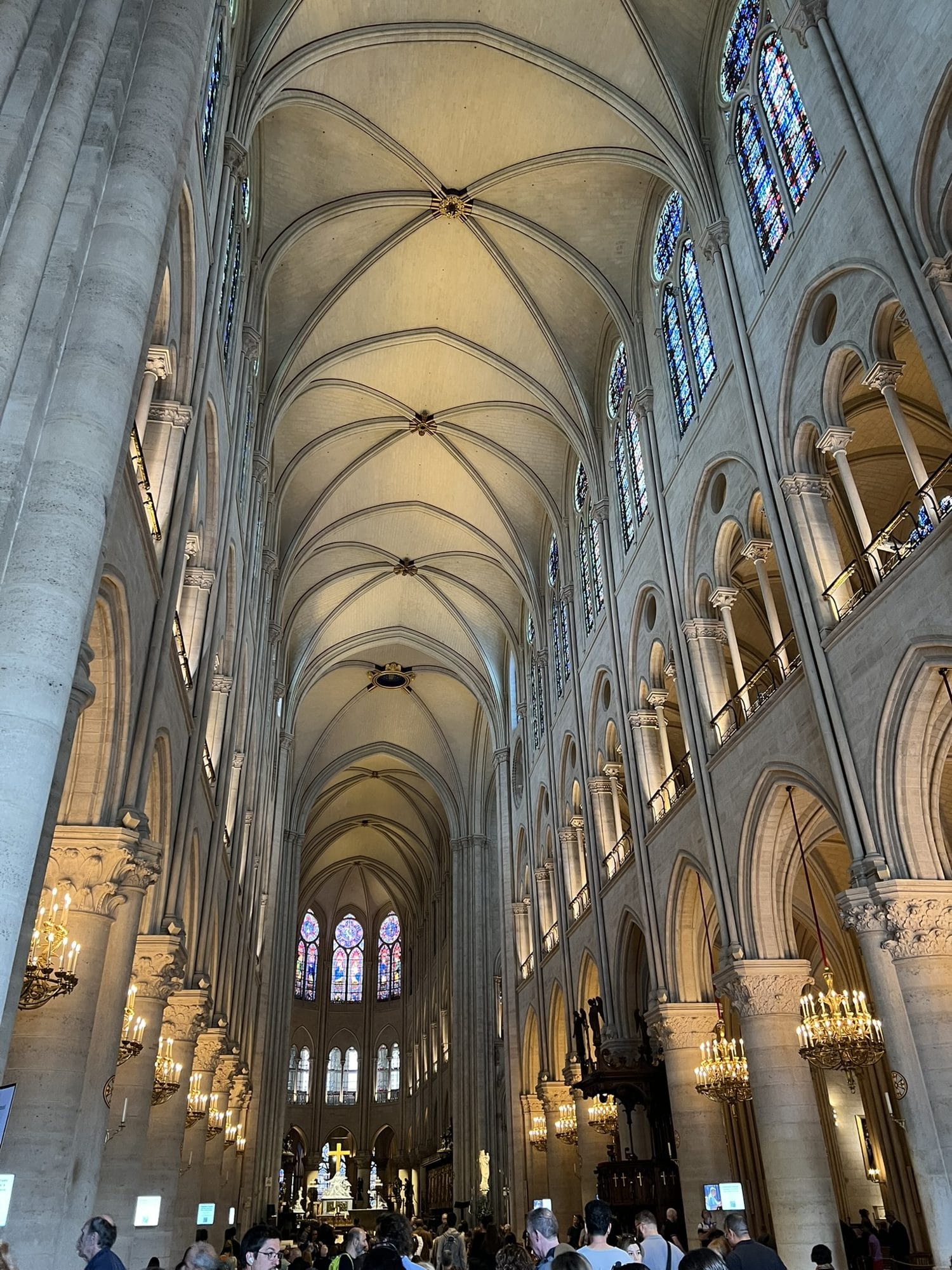 The central nave of Notre-Dame seen from the entrance, with pale vaults and walls after cleaning and visitors in the distance