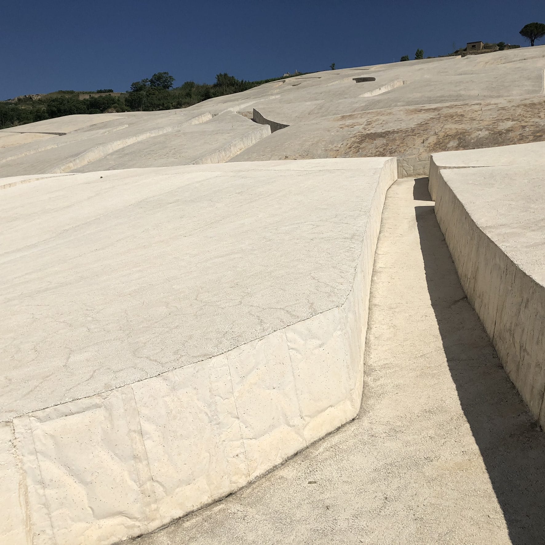 The thick edge of a white concrete block of the Cretto beside a walkway, with the hillside behind