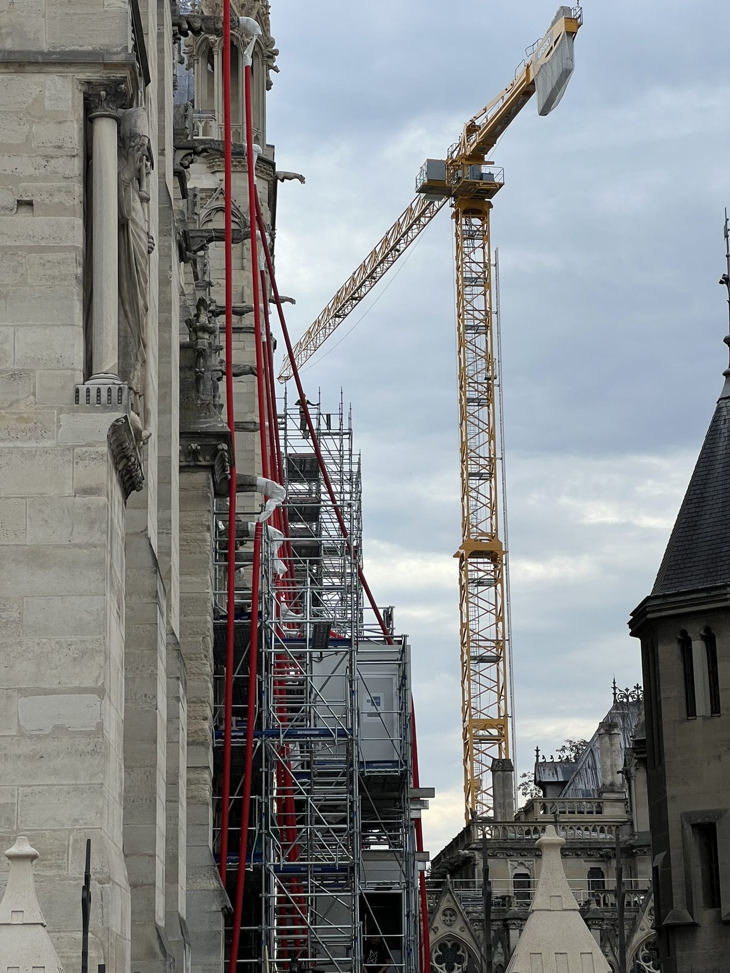 A yellow crane and scaffolding with red netting along the flank of Notre-Dame under a cloudy sky 