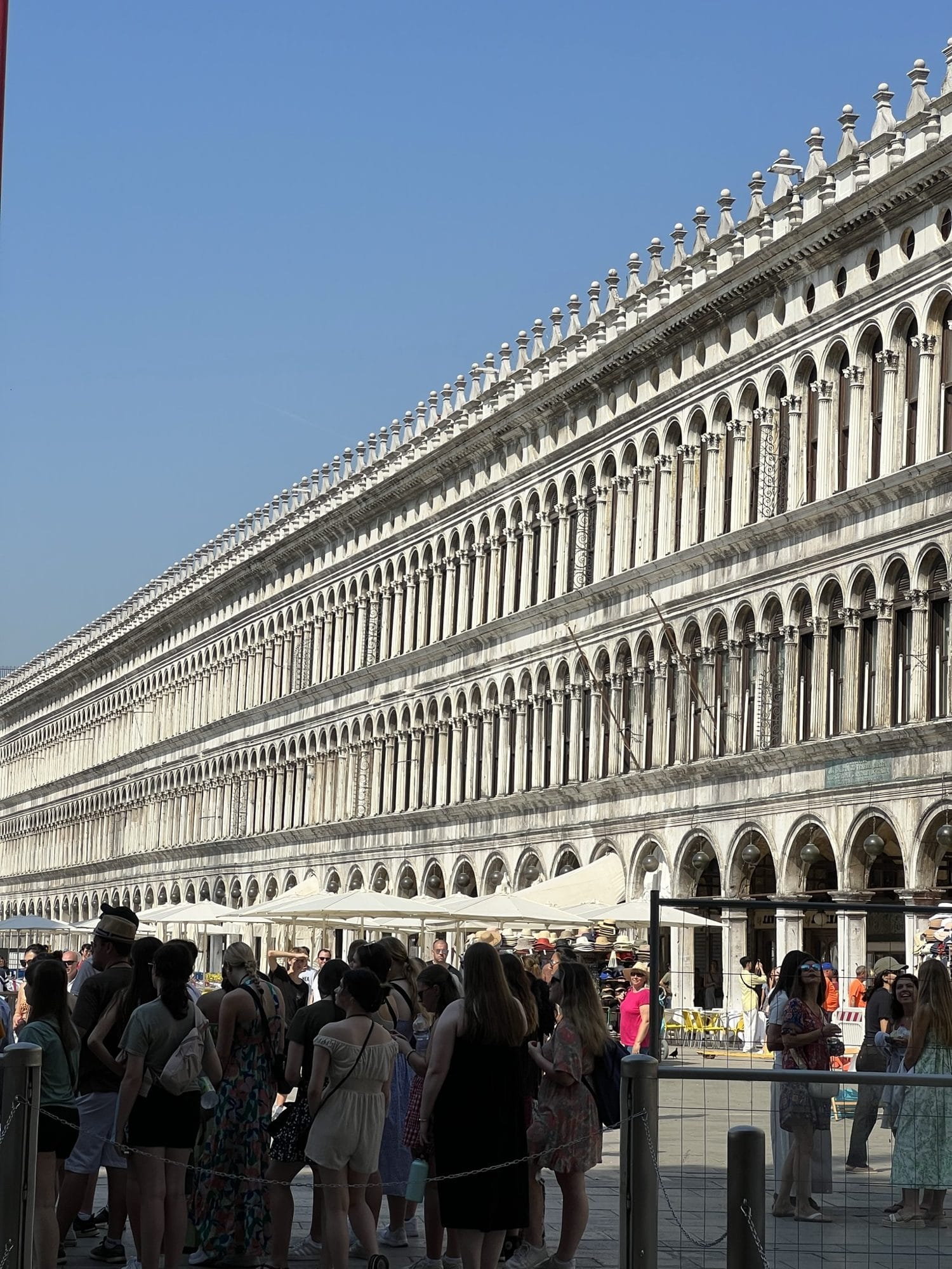 The long arcaded façade of the Procuratie on Piazza San Marco with crowds of visitors along the bottom