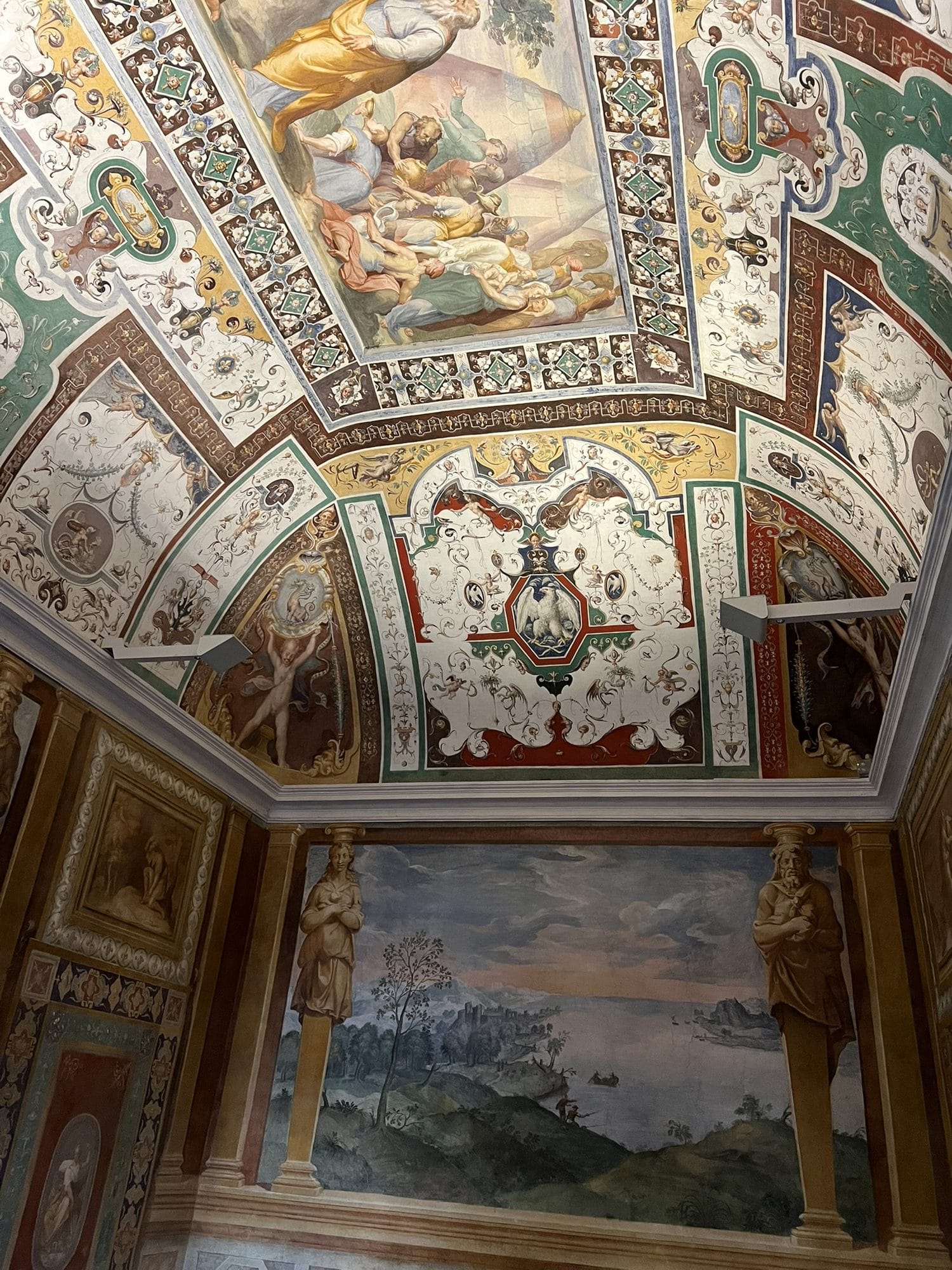 Corner of a frescoed room with painted herms framing a landscape with water, beneath a decorated vault