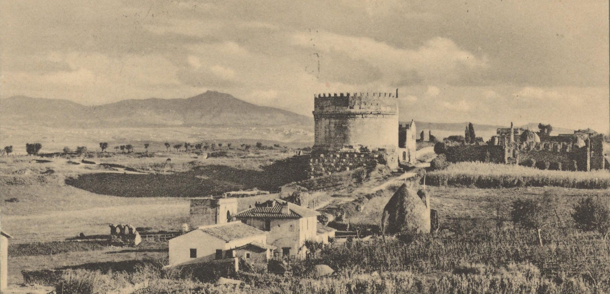 Old sepia postcard of the battlemented tomb of Caecilia Metella above farm buildings and bare fields, with the Alban Hills on the horizon and no rows of trees anywhere