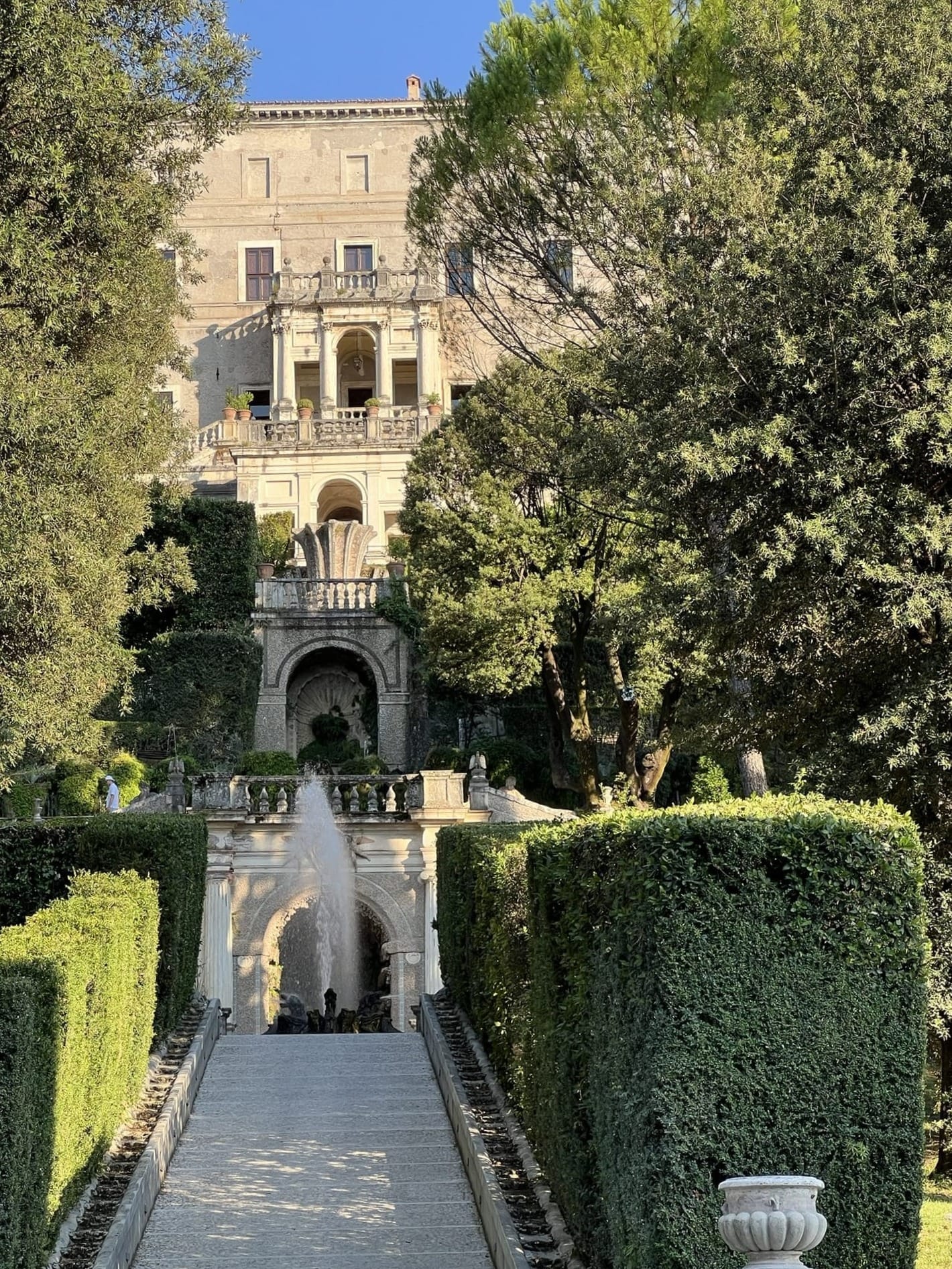 Path between two tall hedges rising towards the loggias and façade of the palace of Villa d'Este