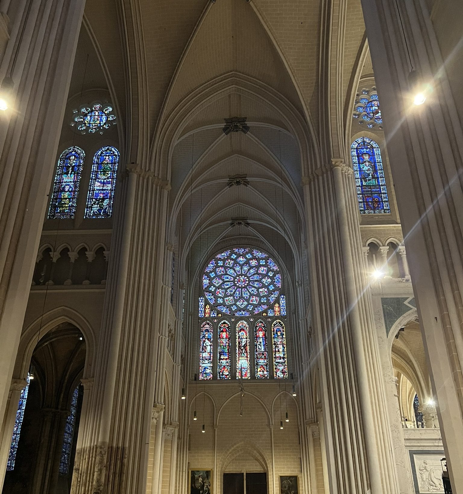 A transept arm of Chartres Cathedral with its rose window and lancets below, while two lit floodlights glare from the piers