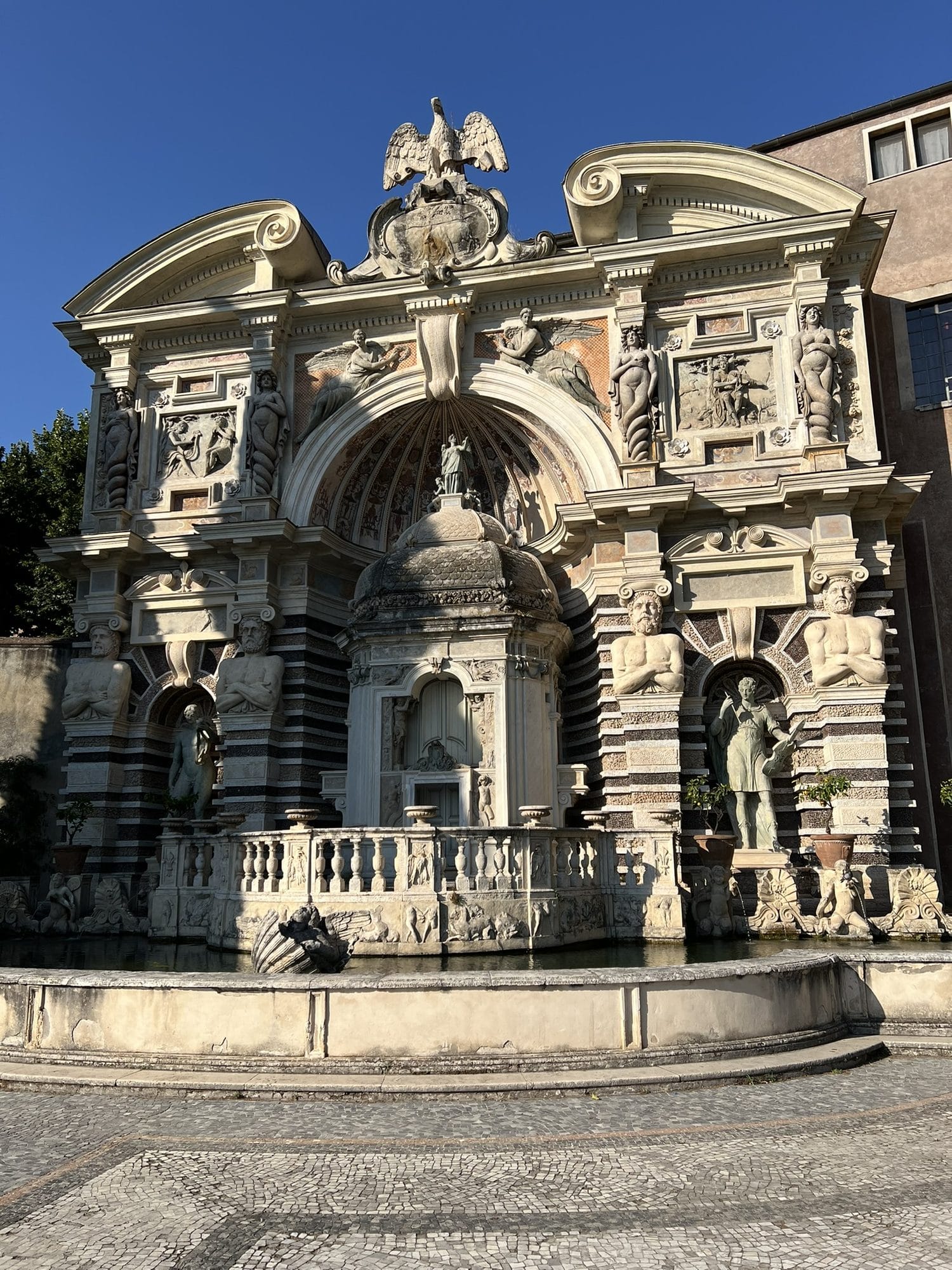 Monumental façade of the Fountain of the Organ with niches, telamons and the Este eagle on top, against a blue sky