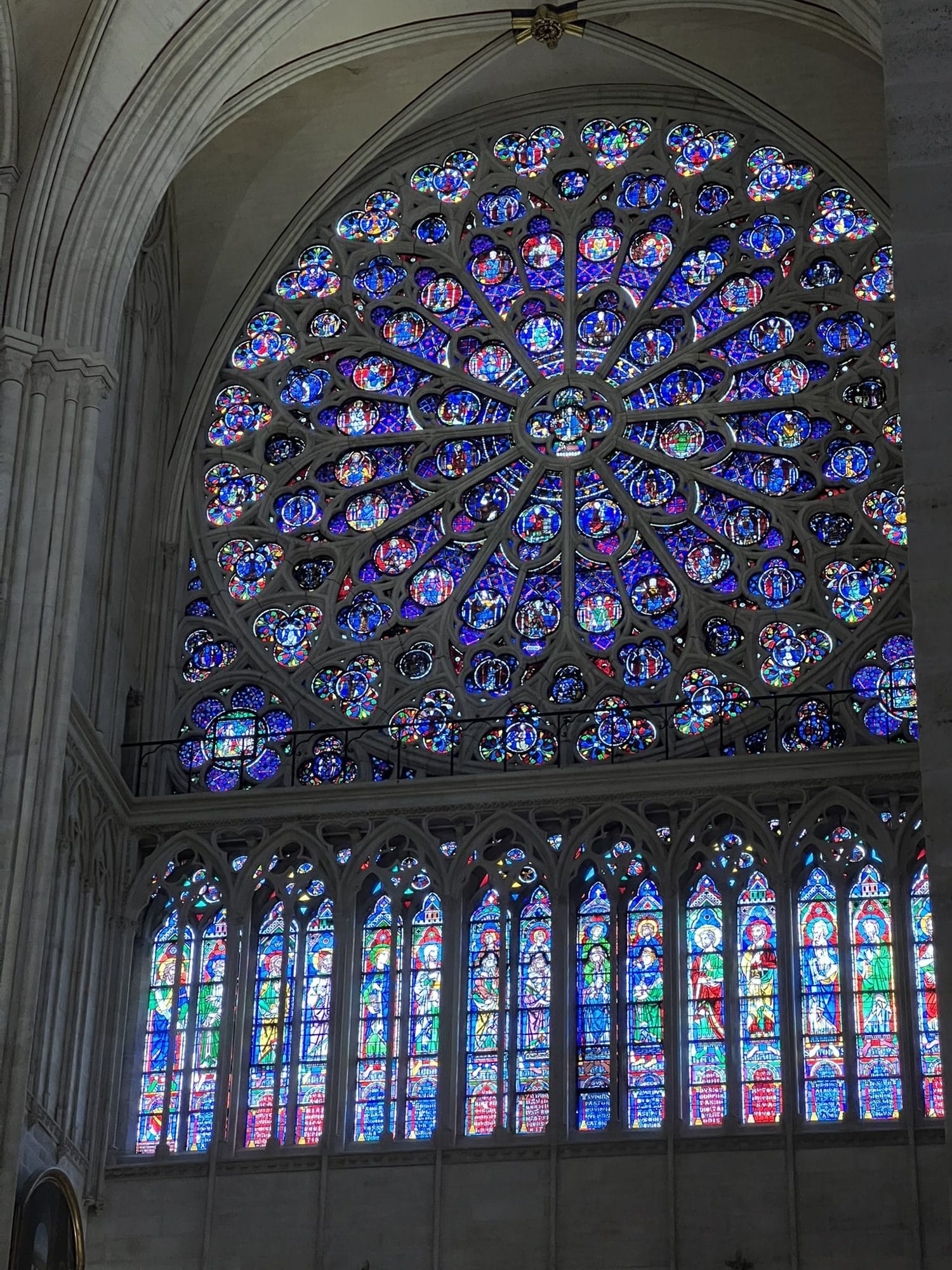 A rose window at Notre-Dame in blues and violets above a row of coloured lancets, set in the stone wall