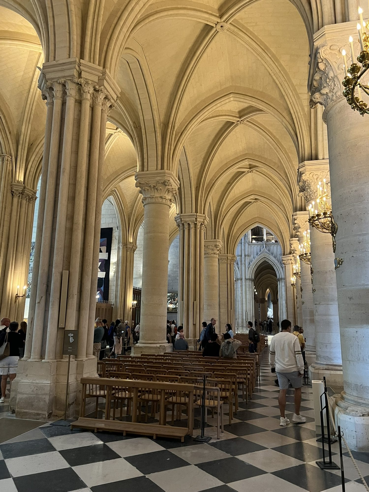 A side aisle of Notre-Dame with cylindrical piers and vaults lit a uniform warm yellow, above a black and white chequered floor