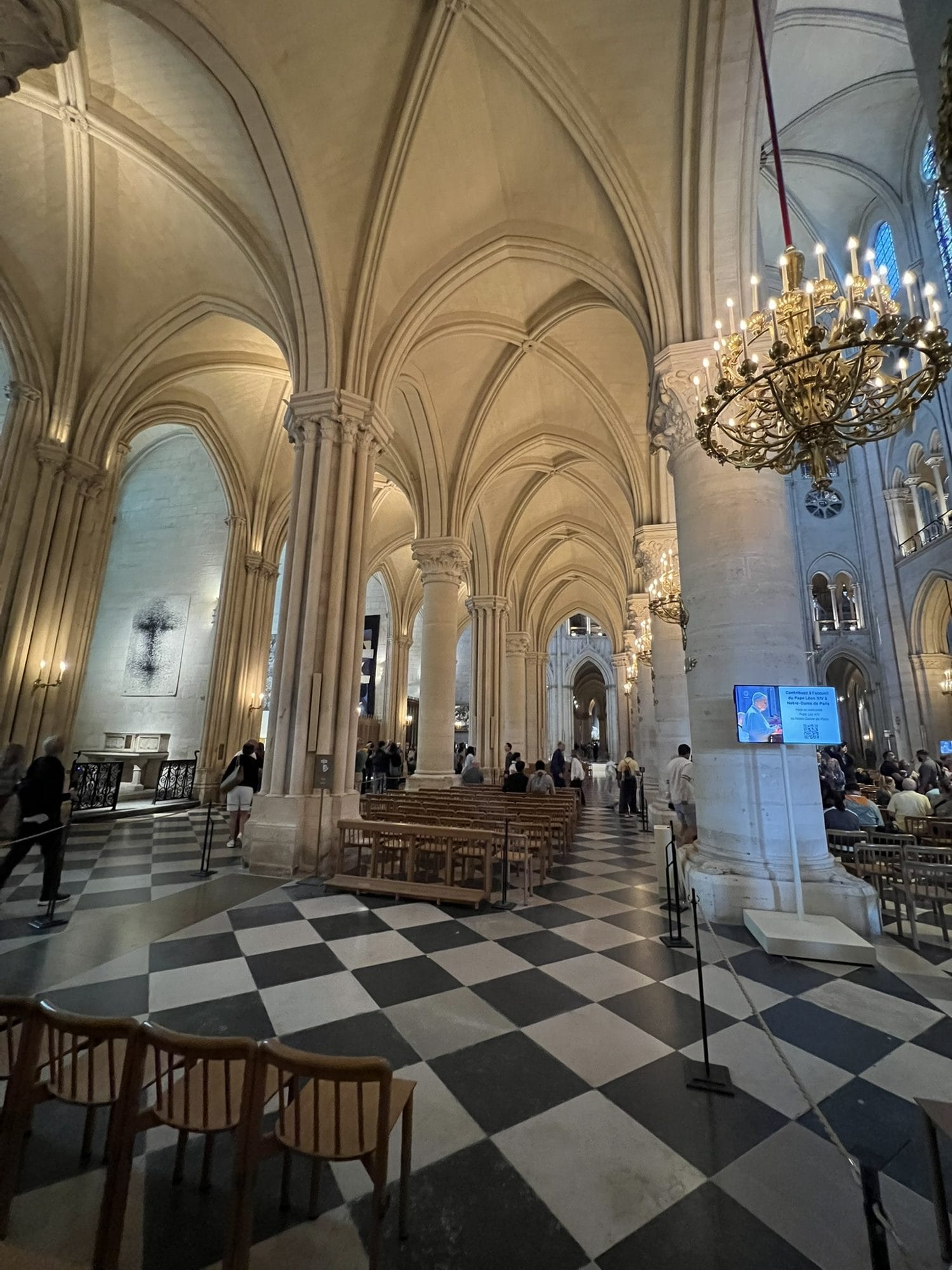 A blue information screen beside a pier in a side aisle of Notre-Dame, against the yellow of the vaults