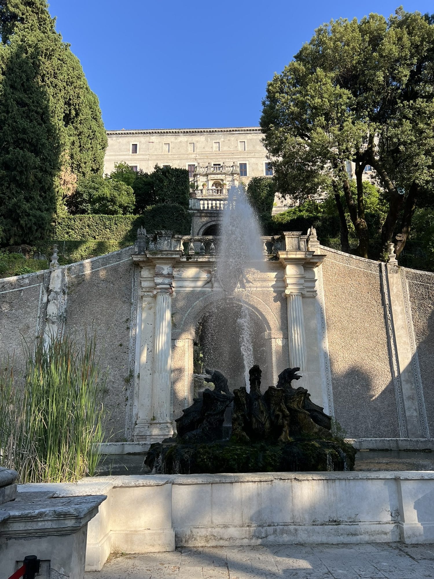 Tall jet of water rising from a sculpted group of dragons in a basin, with stone ramps and the palace in the background