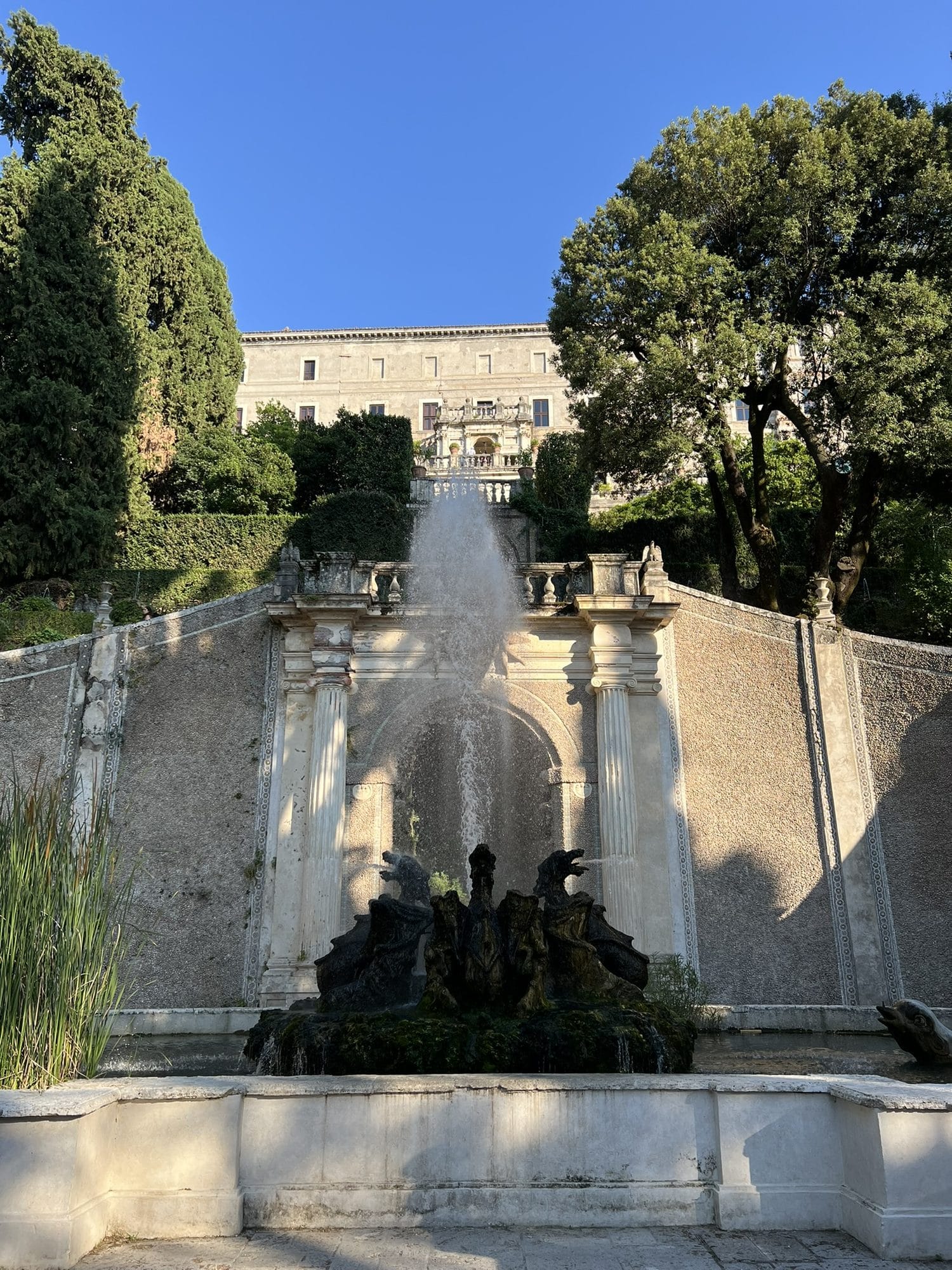 Group of stone dragons at the centre of a basin, with a tall jet of water and the staircase behind