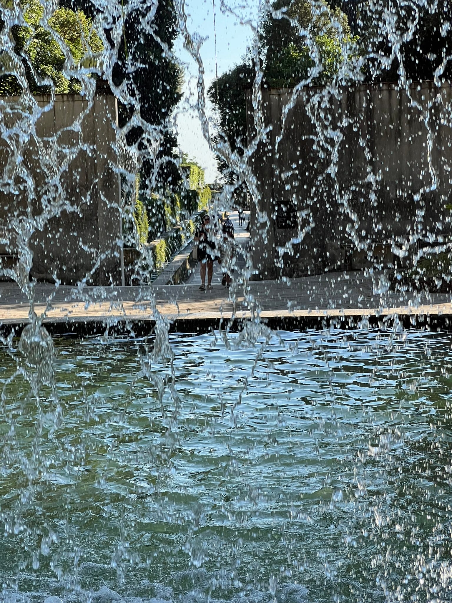View through a curtain of falling water into a pool, with the garden backlit beyond