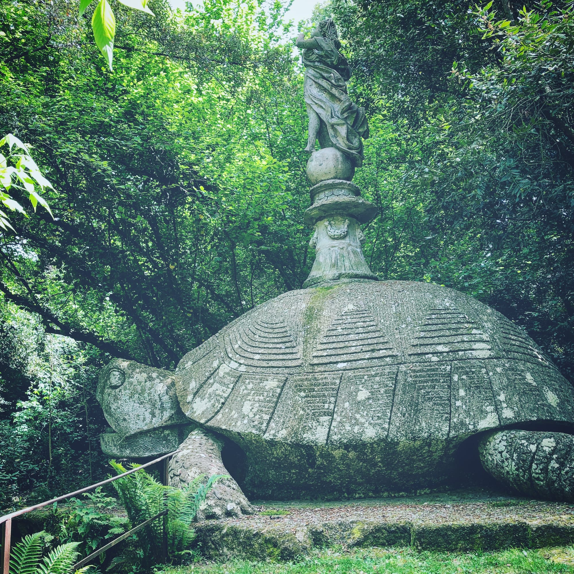 Side view of the giant tortoise sculpture in the Sacro Bosco of Bomarzo, surrounded by fallen leaves and woodland undergrowth.
