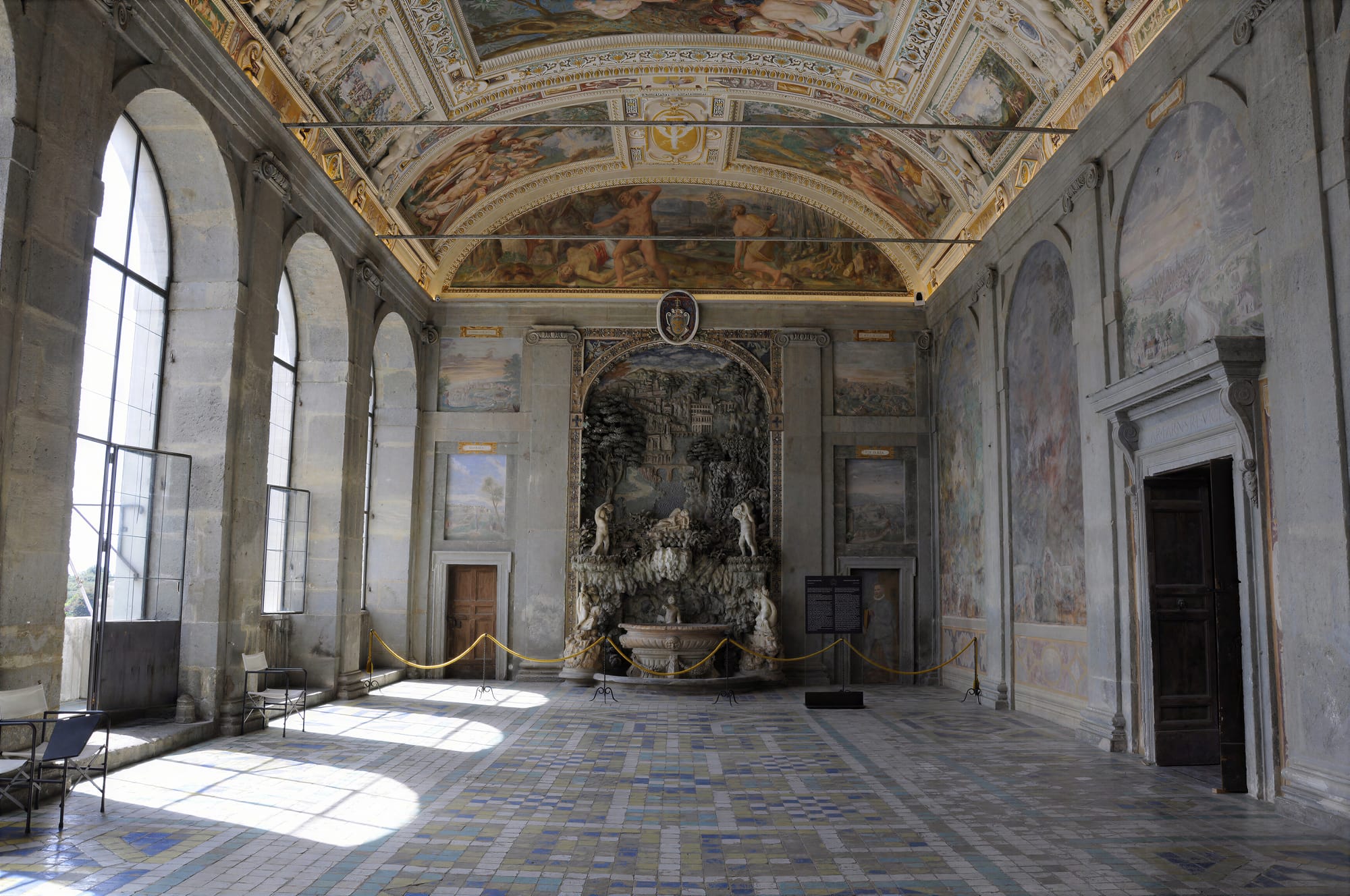 The Sala di Ercole at Palazzo Farnese, Caprarola: arched windows on the left, a rustic fountain at the end wall, landscape views on the walls
