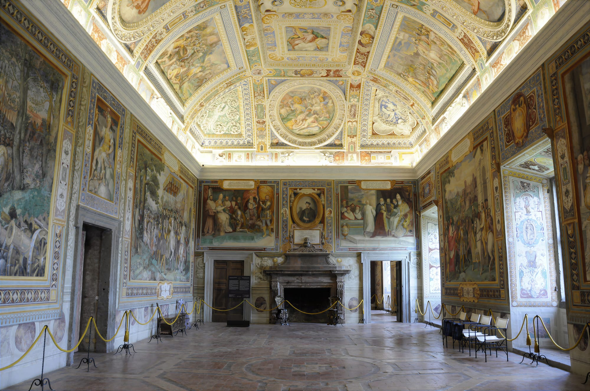 The Sala dei Fasti Farnesiani at Caprarola, a long hall with a frescoed vault, large historical scenes on the walls and a stone fireplace