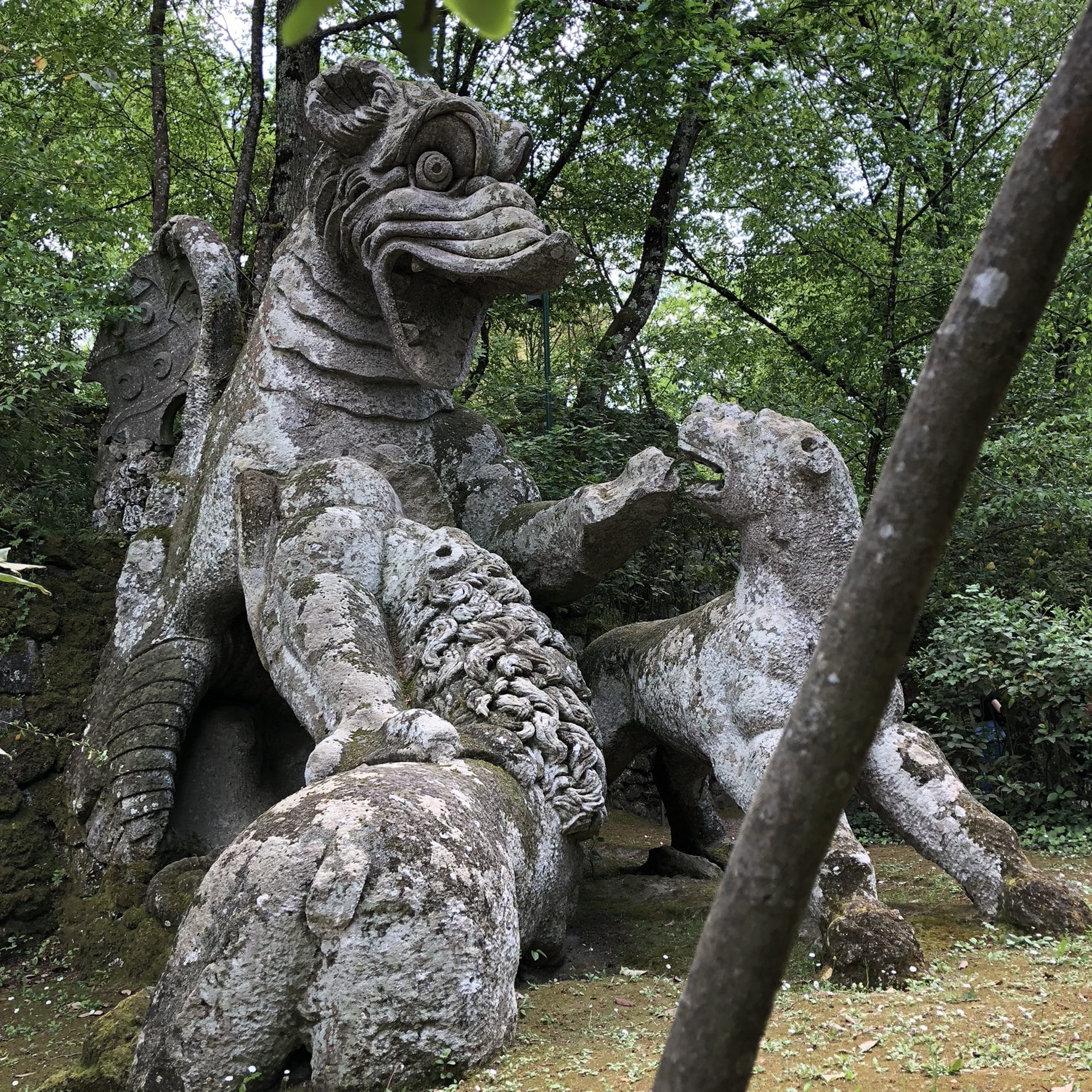 The moss-covered stone dragon of Bomarzo attacked by lions, in the green undergrowth