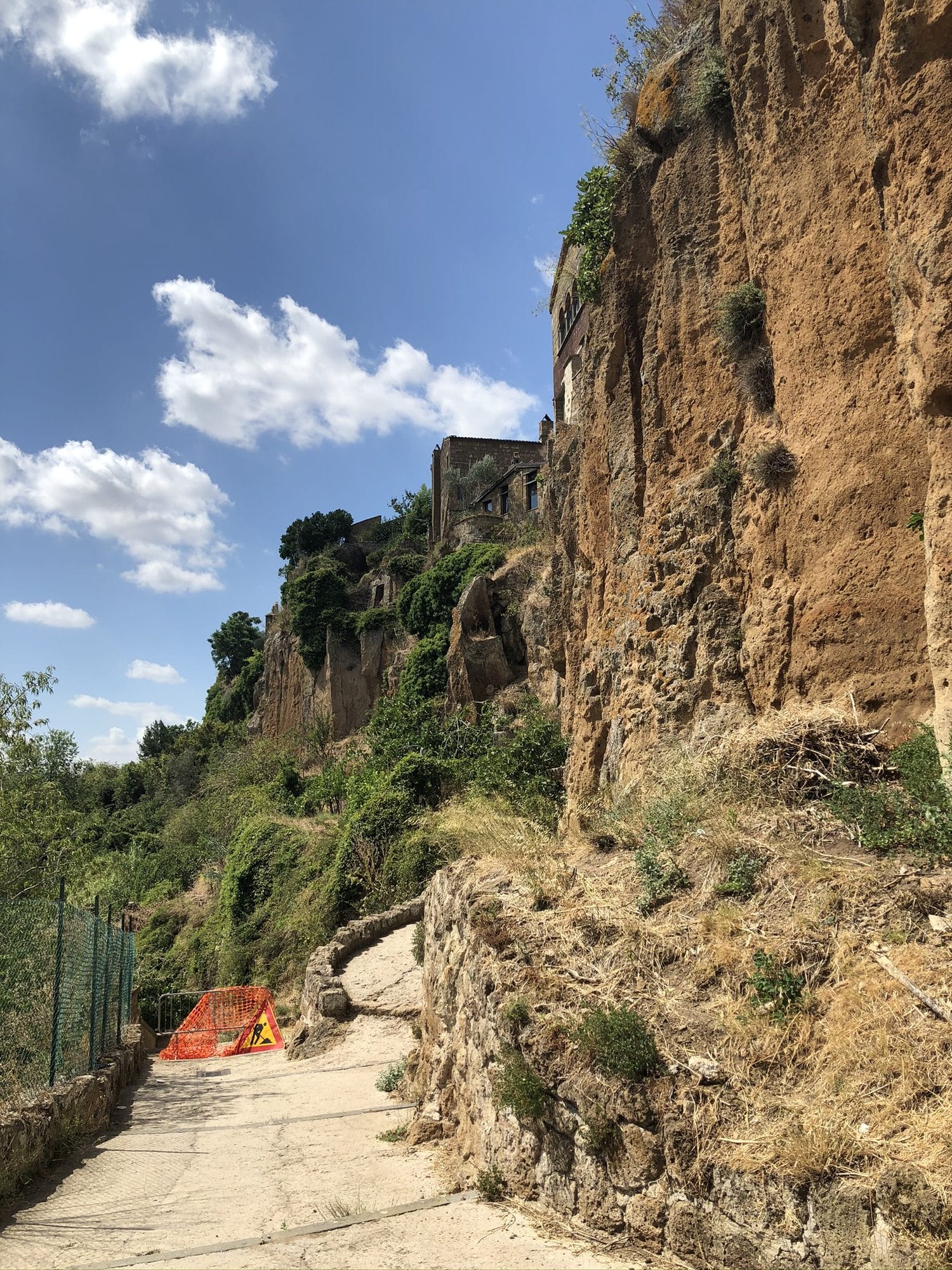 The tufa cliff below Civita di Bagnoregio with an orange construction fence at its base, blue sky above