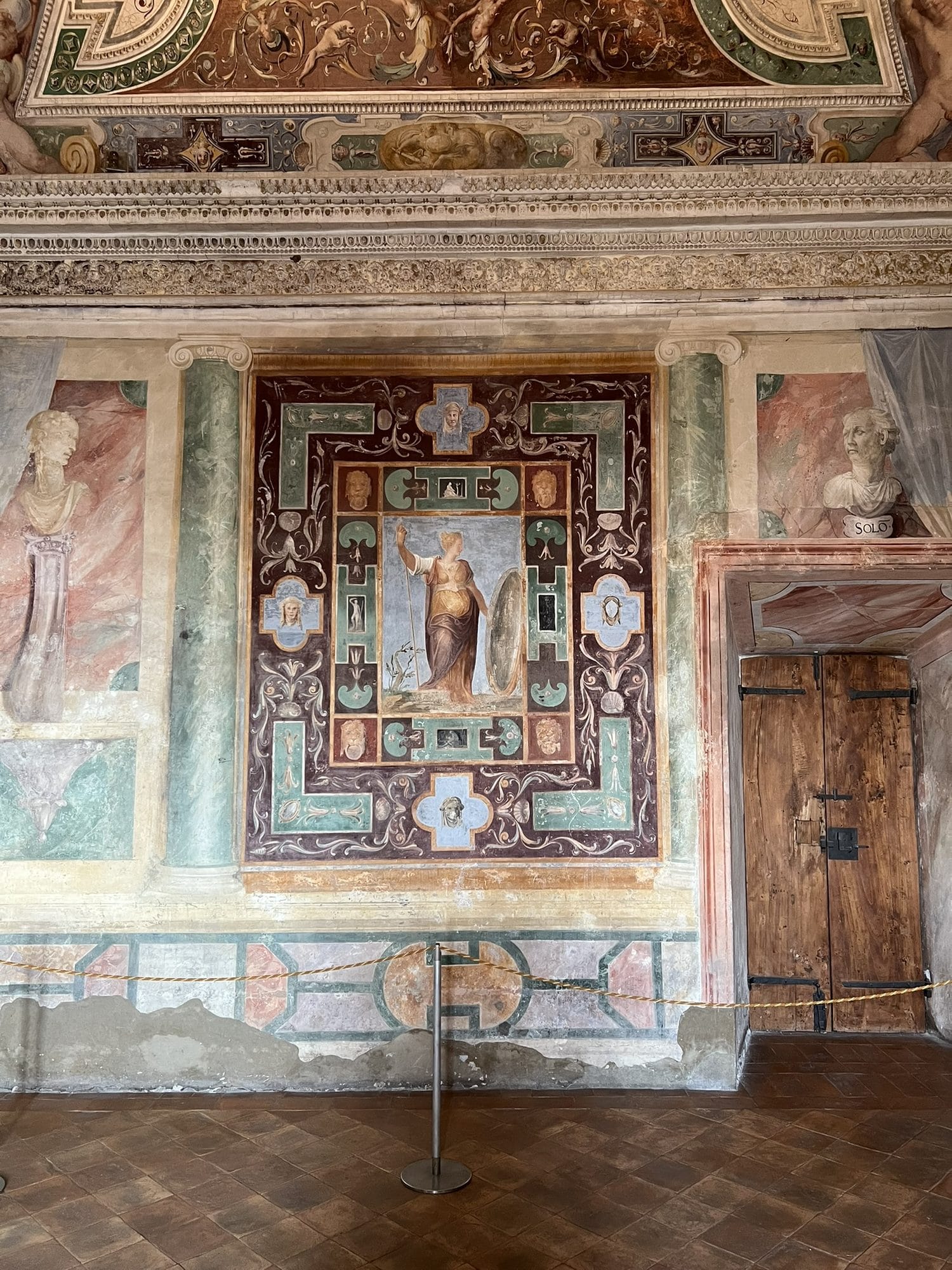 Painted room in the palace of Villa d'Este: frescoed walls with fake frames and a painted bust beside a wooden door 