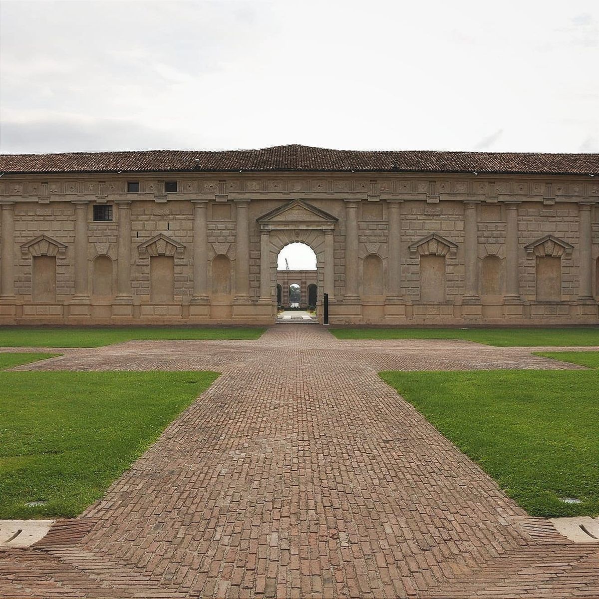 Symmetrical view of the interior Courtyard of Honor with a brick pathway crossing a green lawn.