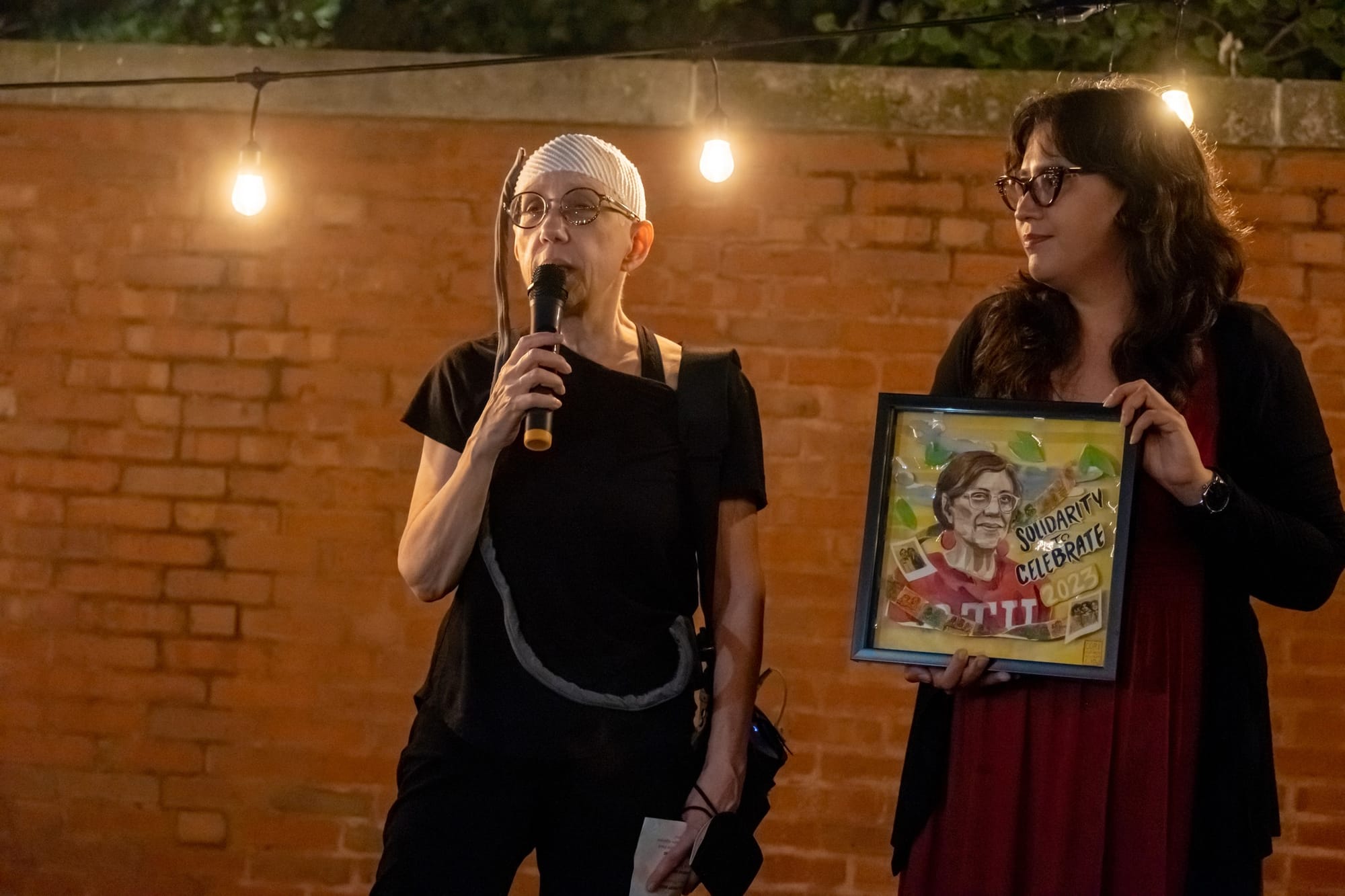 Kelly stands alongside Chris Geovanis. Kelly is holding artwork that was made in Christine's honor.