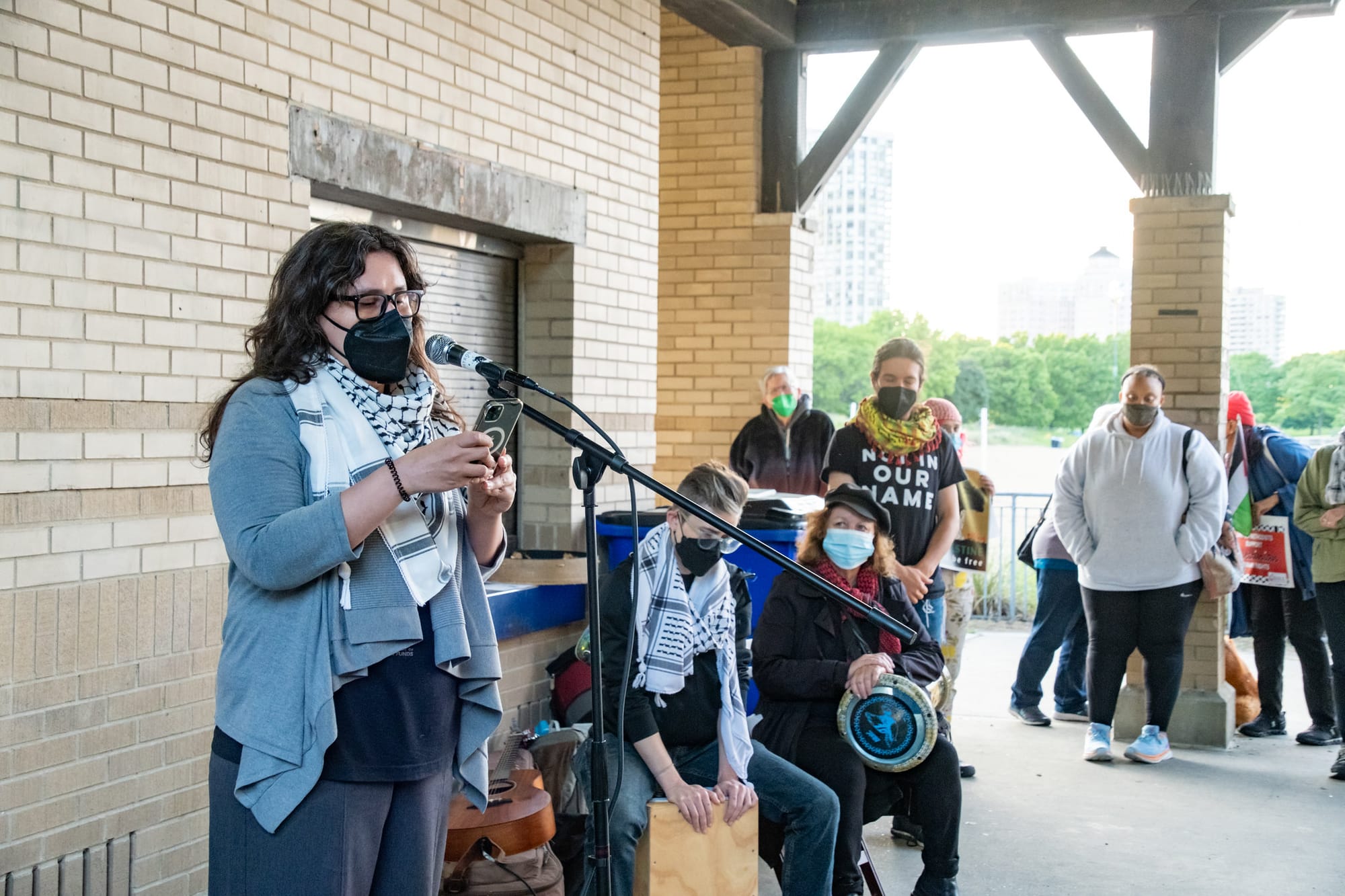 Kelly Hayes stands beside musicians and addresses a crowd.
