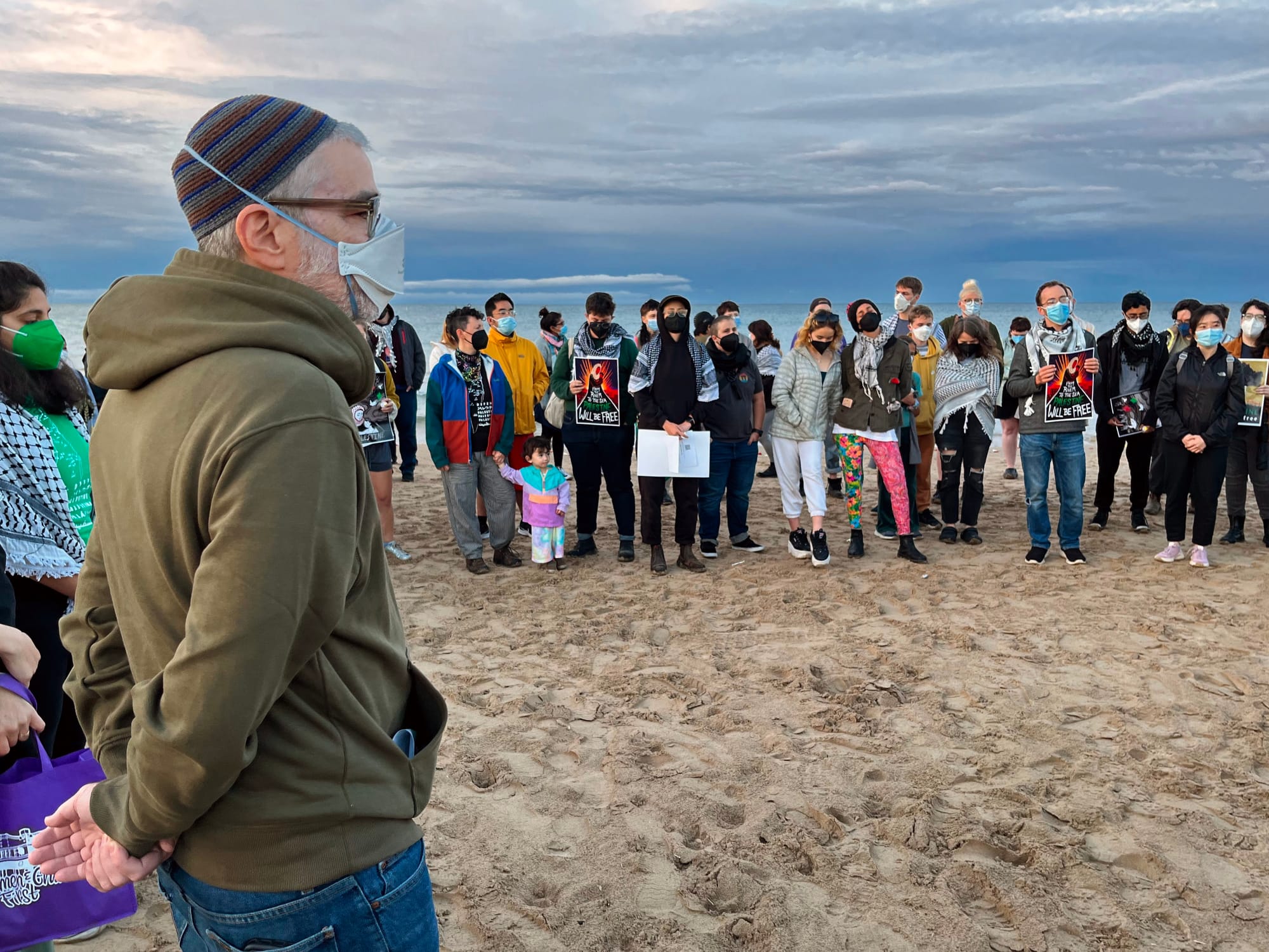Mourners hold Palestine solidarity signs on a beach.