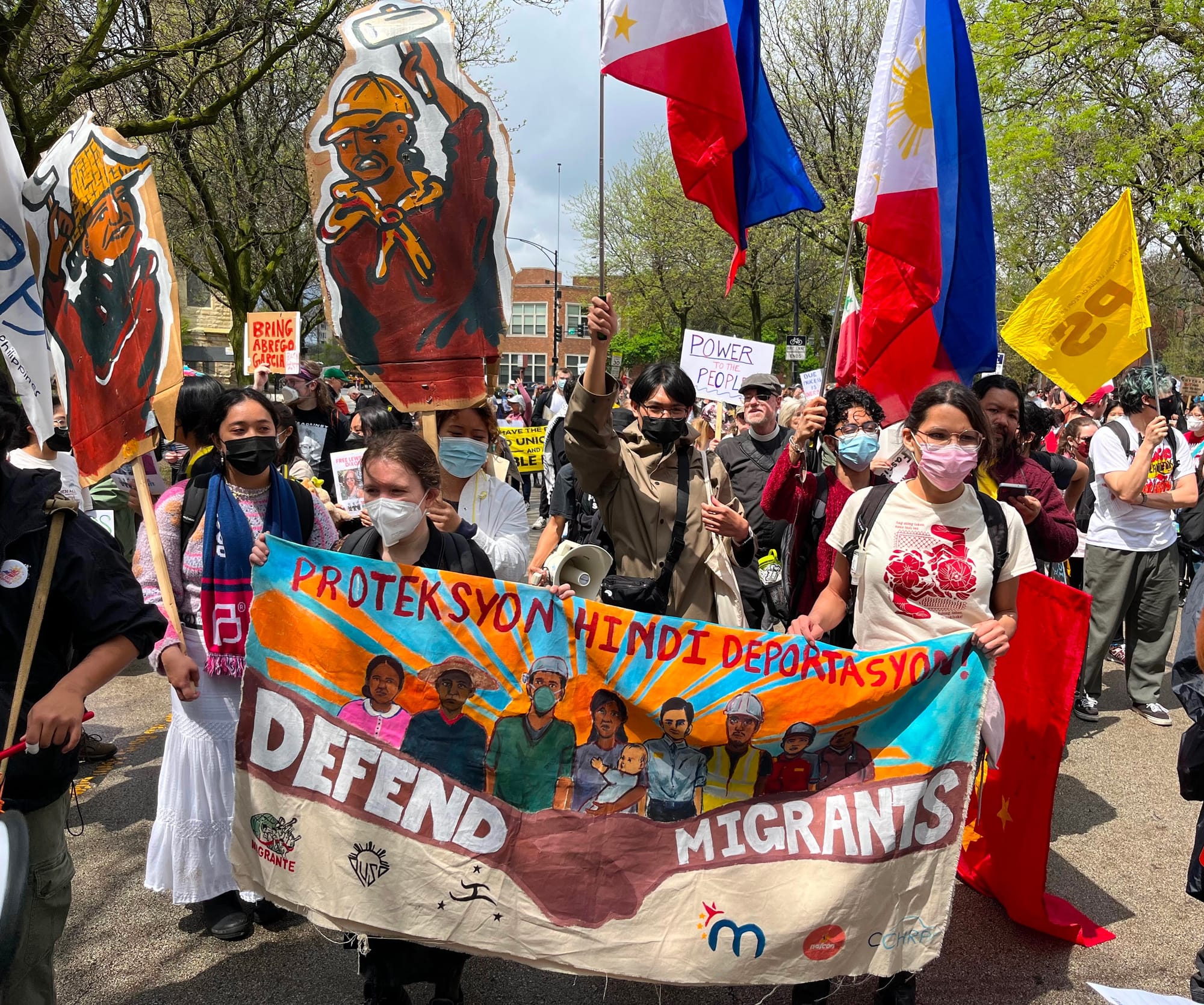 Protesters hold a banner that says, "Defend Migrants."
