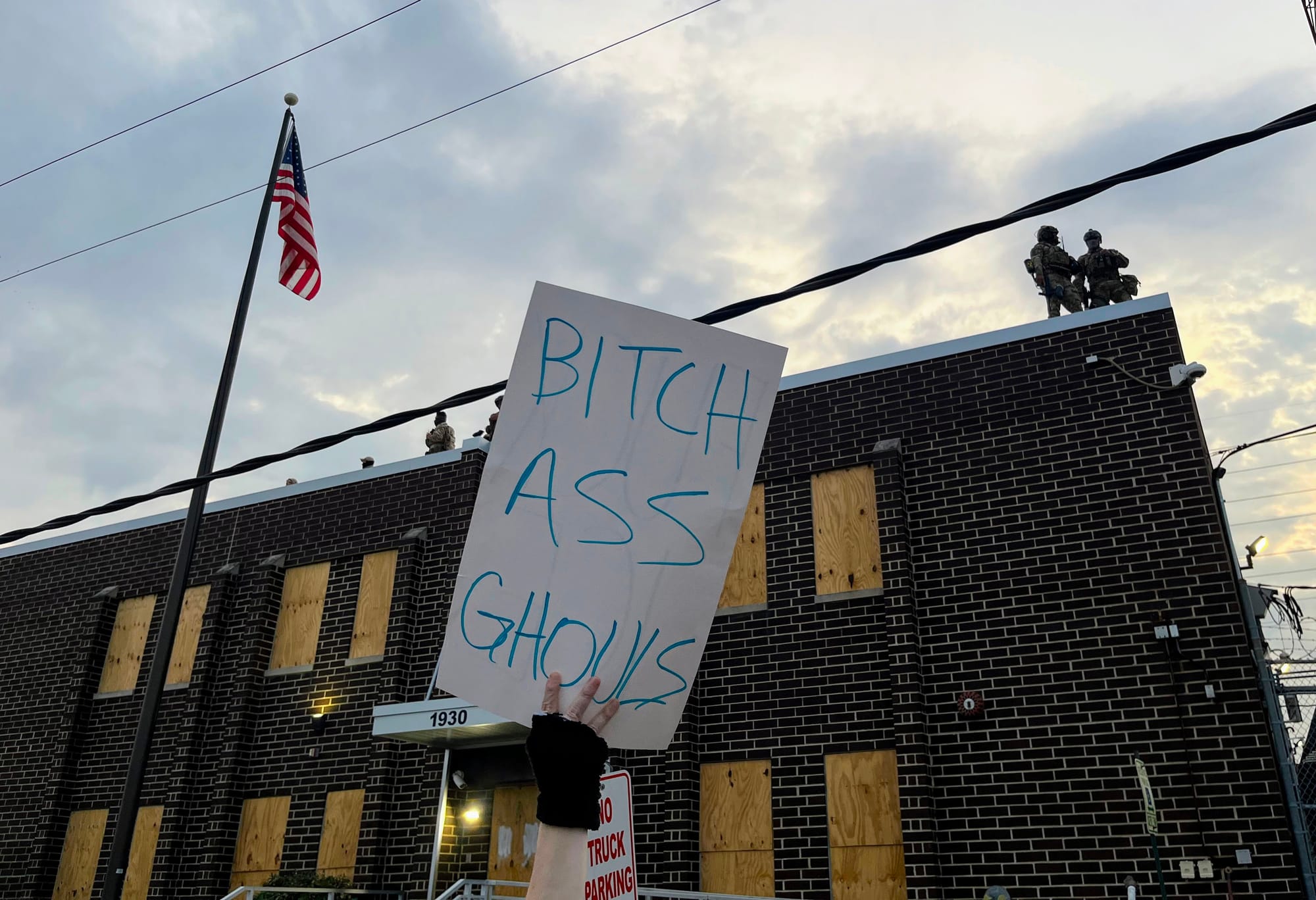 A protester holds a sign that reads: "Bitch ass ghouls" outside an ICE facility.