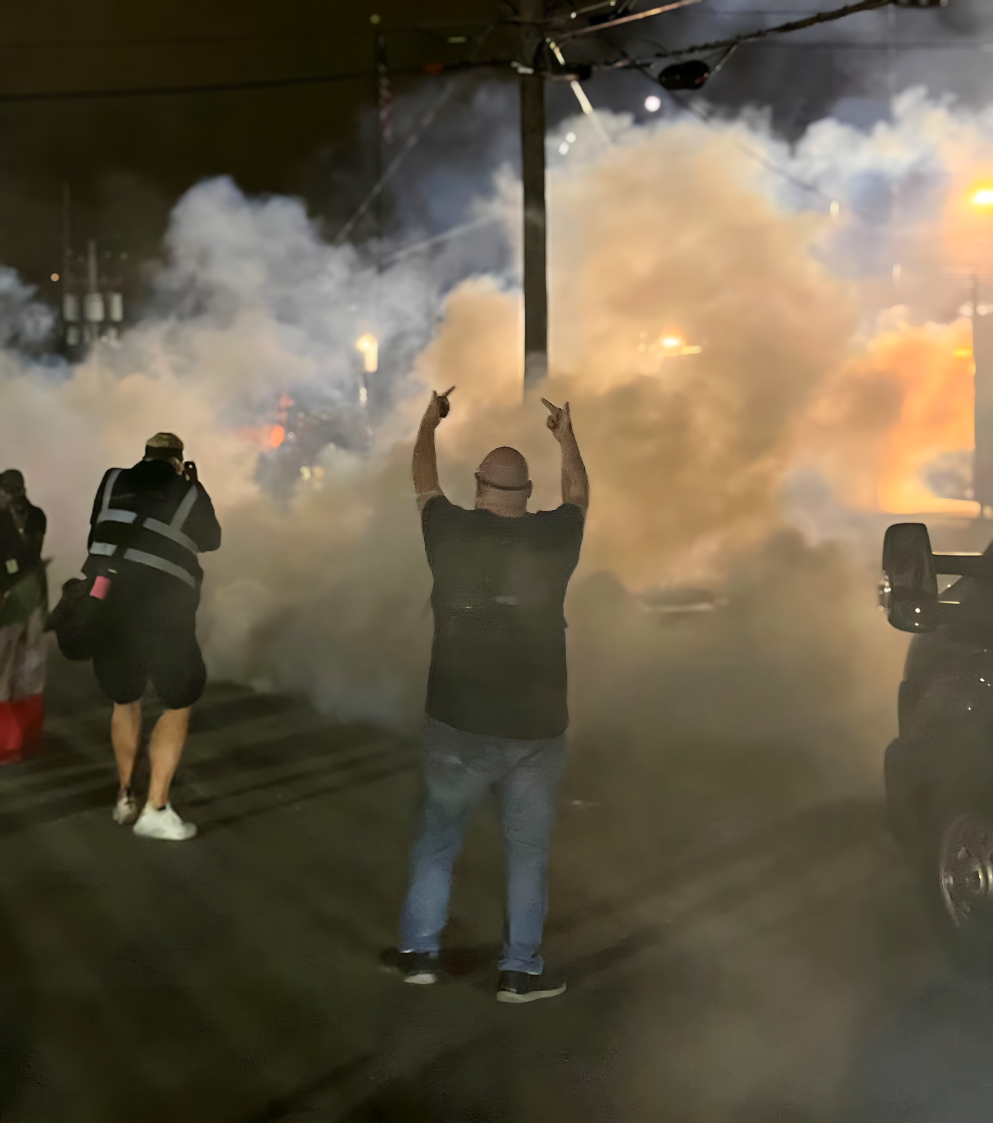 A man holds up his middle fingers amid clouds of tear gas.