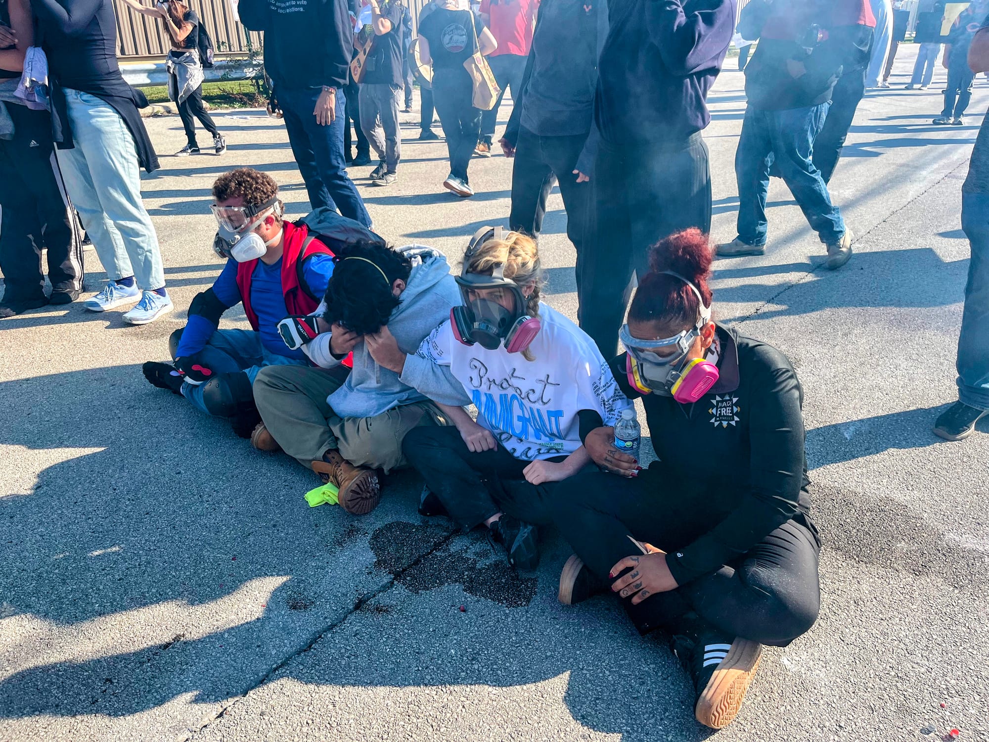 Protesters sit with their arms locked as tear gas wafts through the street.