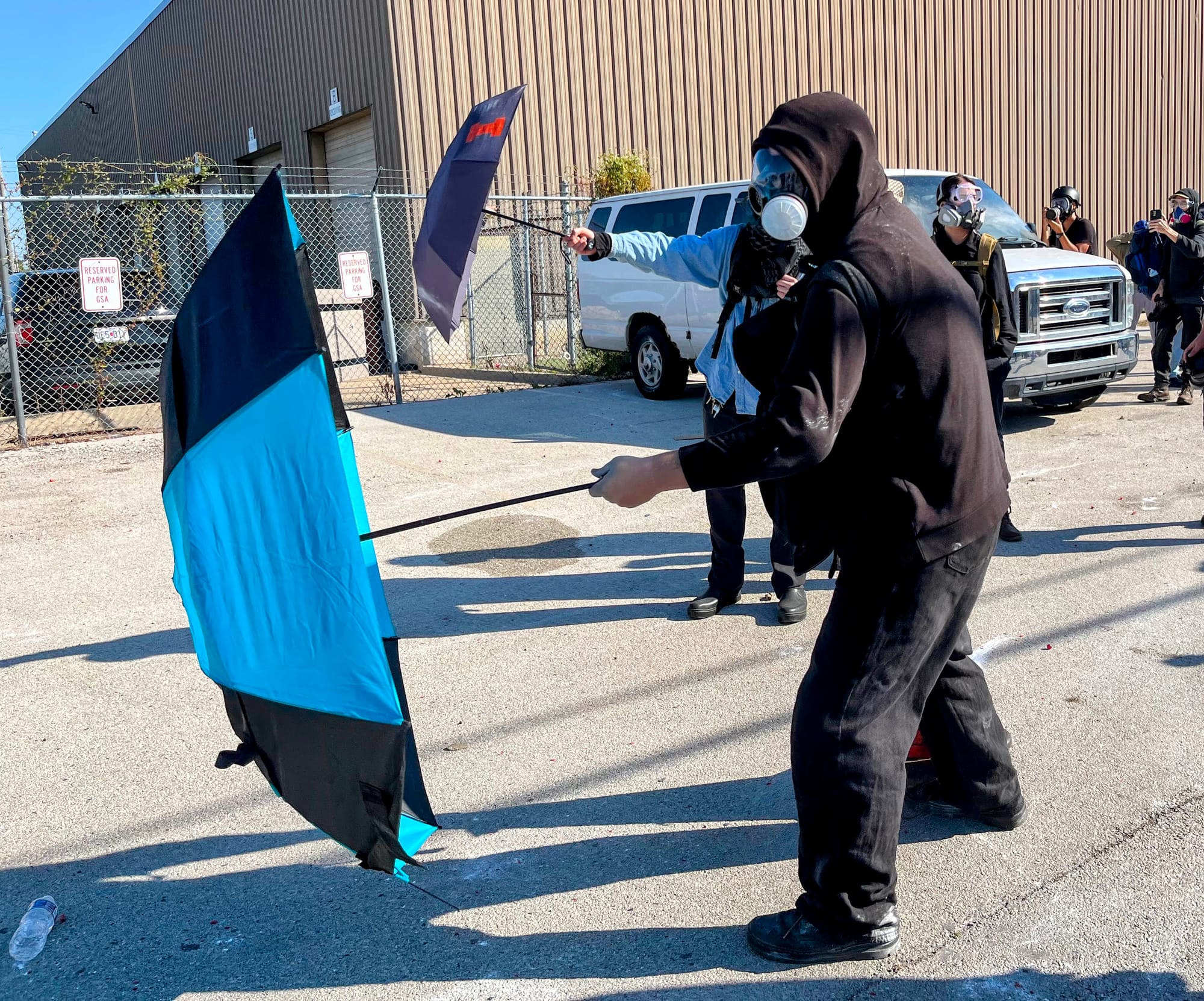 A protester in a gas mask holds out an umbrella as a shield.