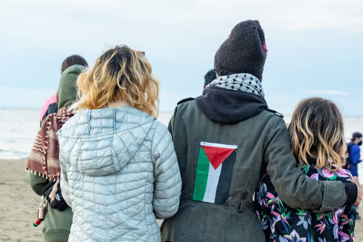 A group of mourners comfort each other. One wears a small Palestinian flag on their back.