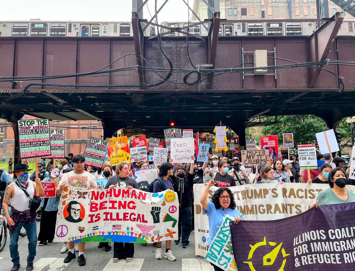 A crowd of protesters march under and elevated train.