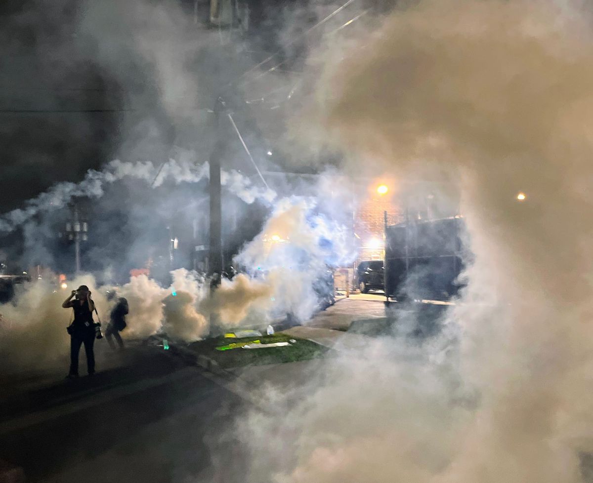 Tear gas streams through the air as a protester puts on their gas mask.