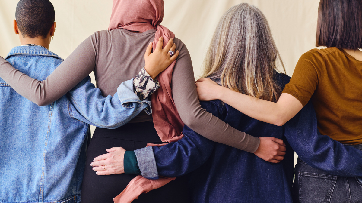 A diverse group of people stand side by side with their arms grasping each other's backs.