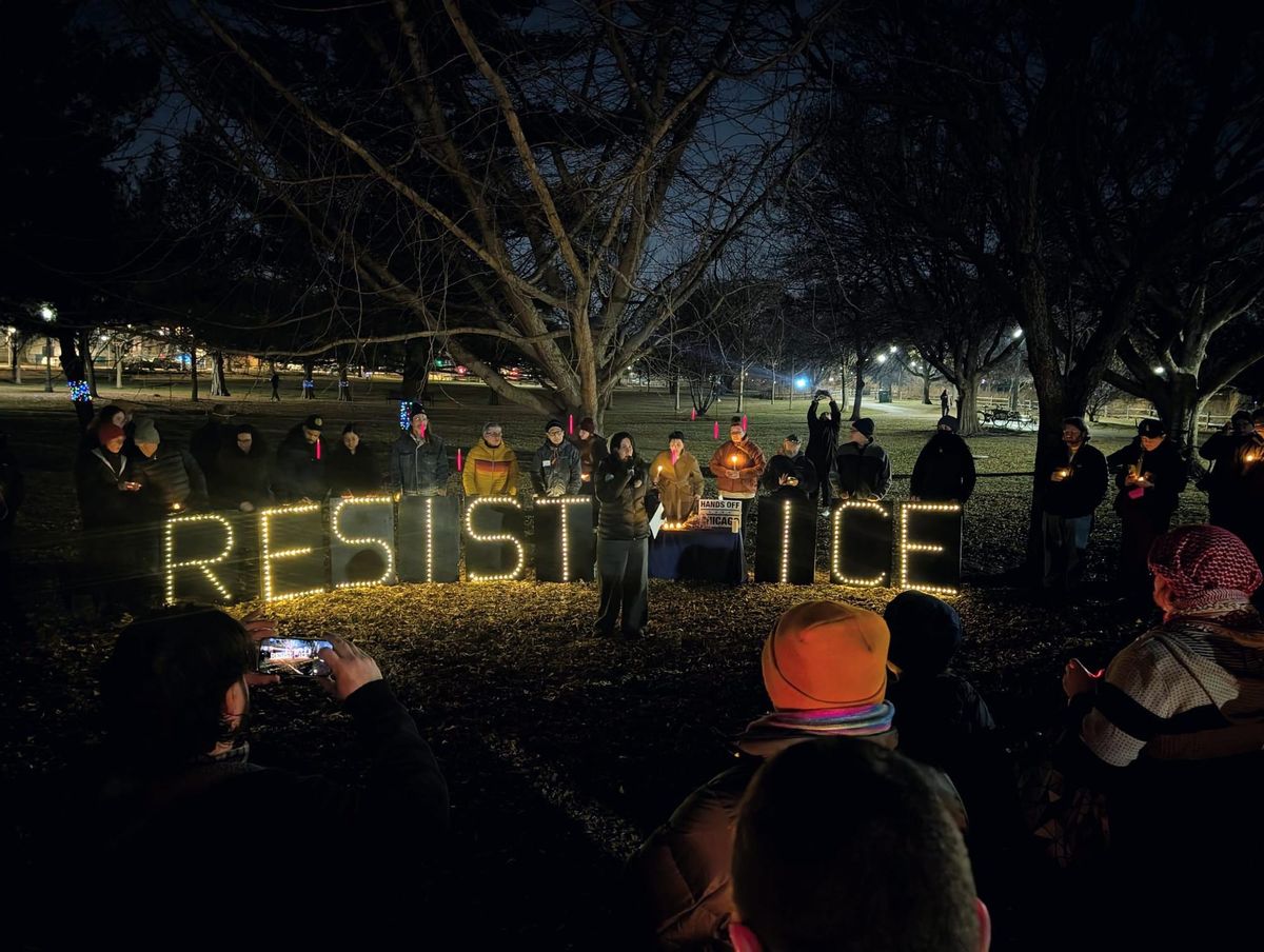 Kelly Hayes speaks to a crowd in front of protesters holding lighted signs that read: "RESIST ICE."