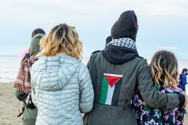 A group of mourners comfort each other. One wears a small Palestinian flag on their back.