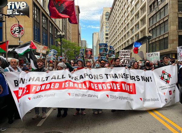Palestine solidarity protesters block an intersection while holding a banner, signs and Palestinian flags.