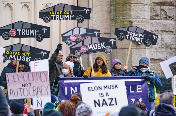 Protesters at a Tesla Takedown protest in Chicago hold anti-Musk signs shaped like Cybertrucks.