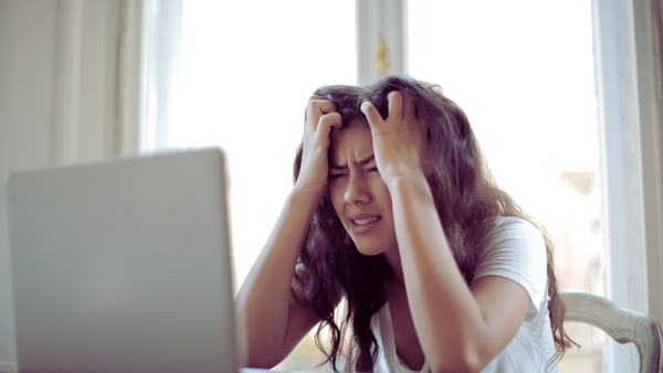 A woman grasps her hair and forehead in frustration while staring at a computer.
