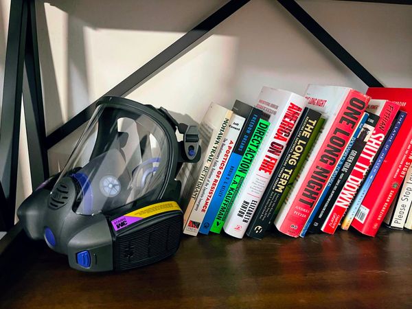A gas mask sits on a book shelf beside poetry books and social justice texts.