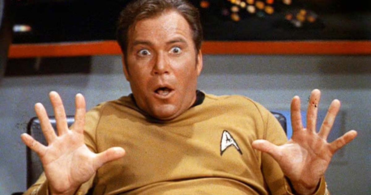 Captain Kirk, played by William Shatner, appears surprised, raising both hands.
