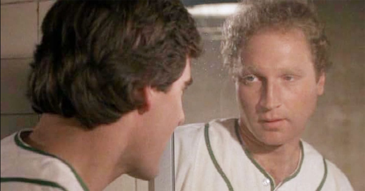 A man in a baseball uniform sees a different face reflected back at him.